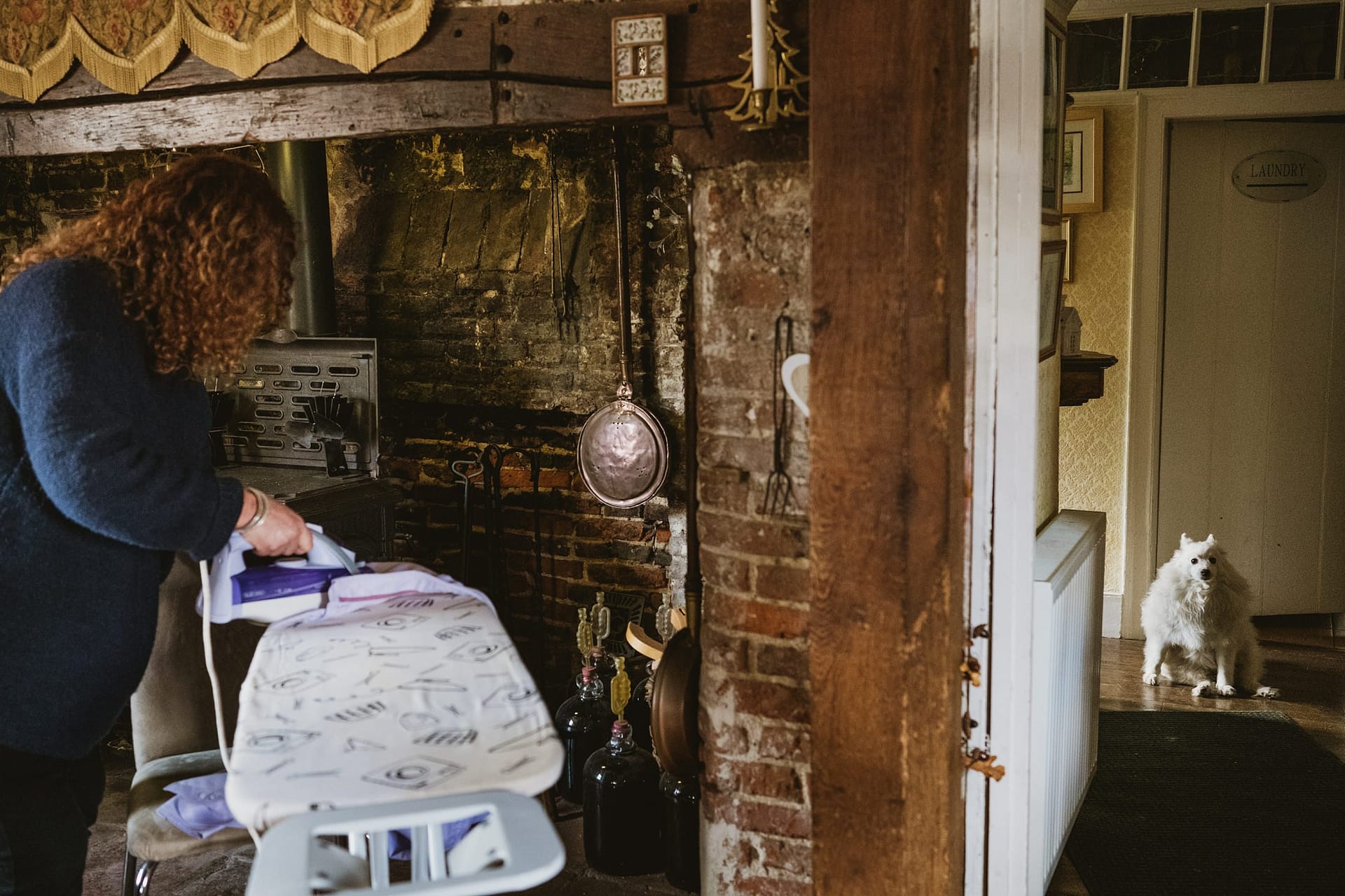 white dog staring at photographer whilst mother of groom irons at Alpheton Barns