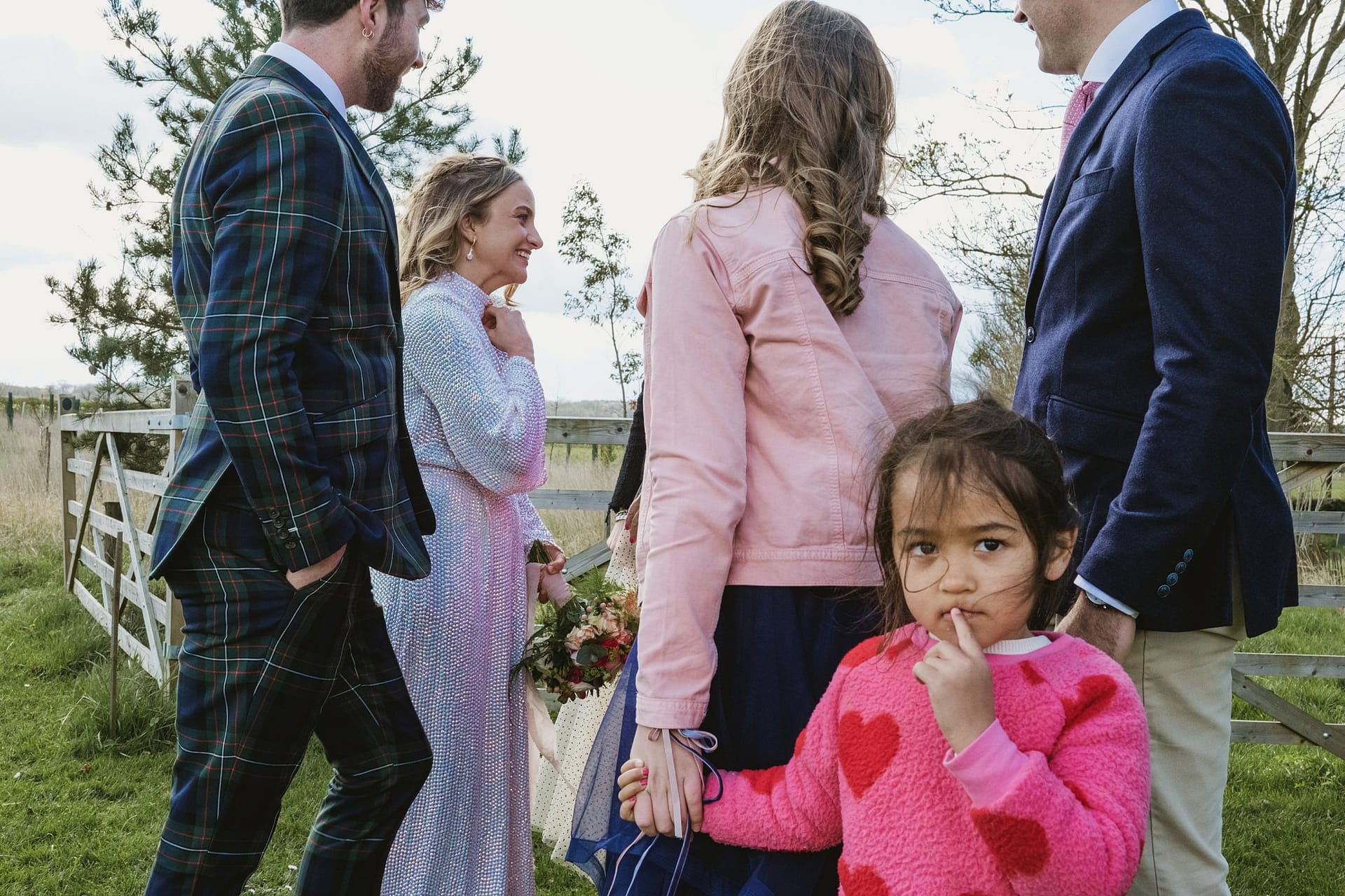 Alpheton Barns suffolk wedding reception, little girl looks at camera with bride and guests in background