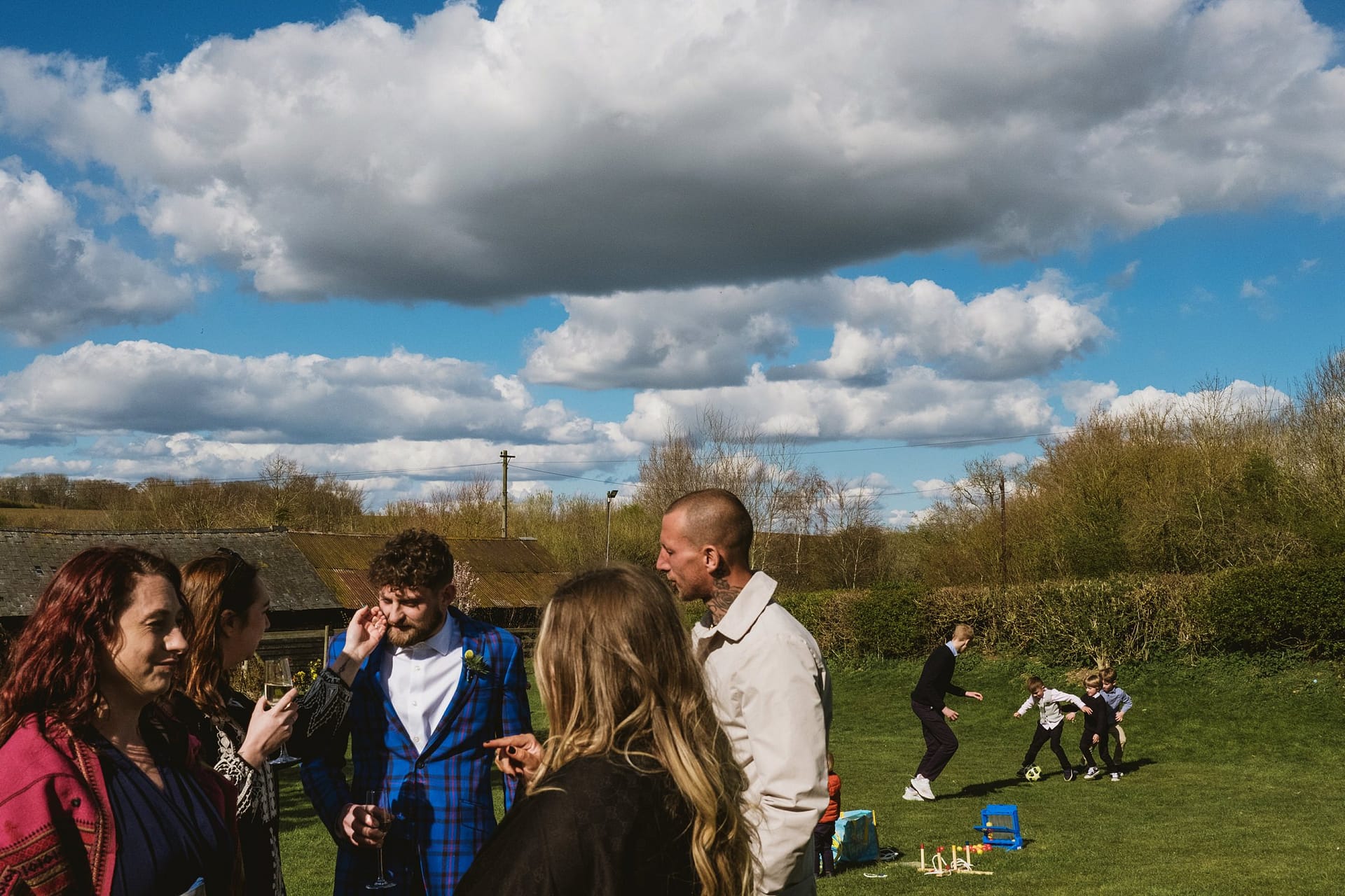 wedding guests chatting whilst children playing in background at Alpheton Barns in suffolk