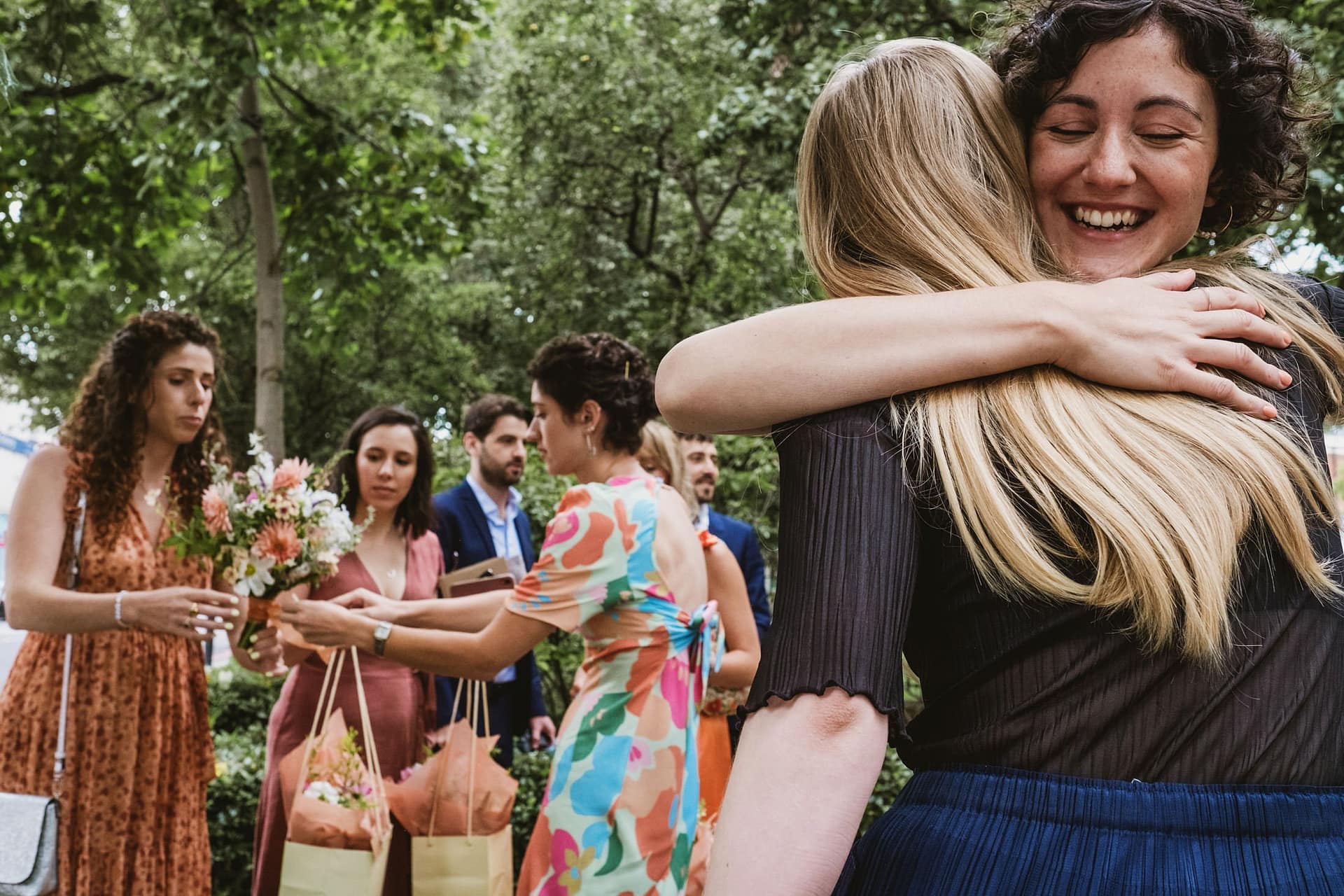 bride hugging wedding guest outside Islington Town Hall before the ceremony and wedding guests hand out flowers in the background
