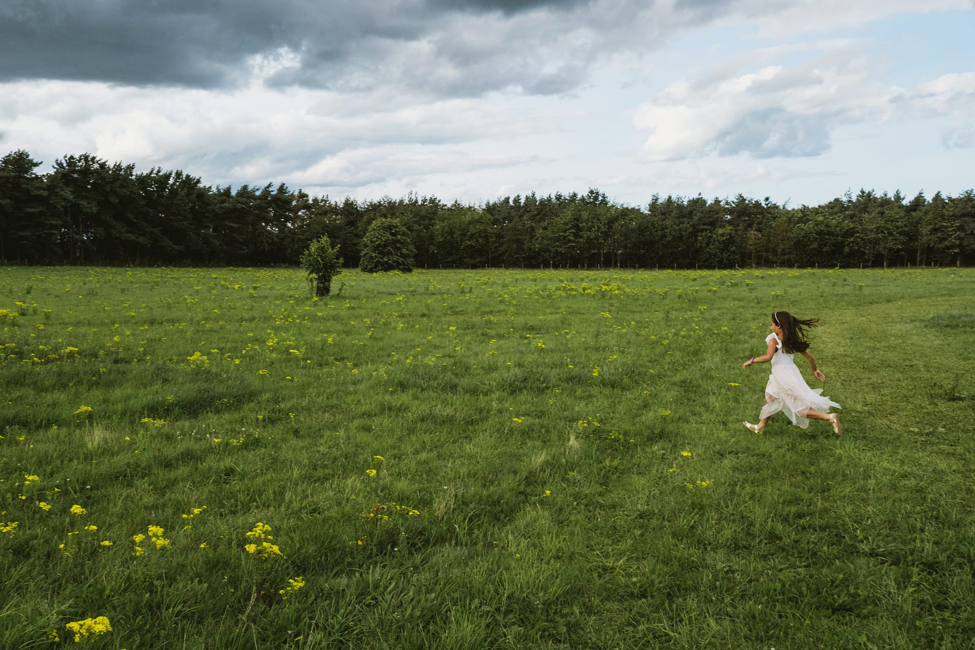 Child running in green meadow under cloudy sky.