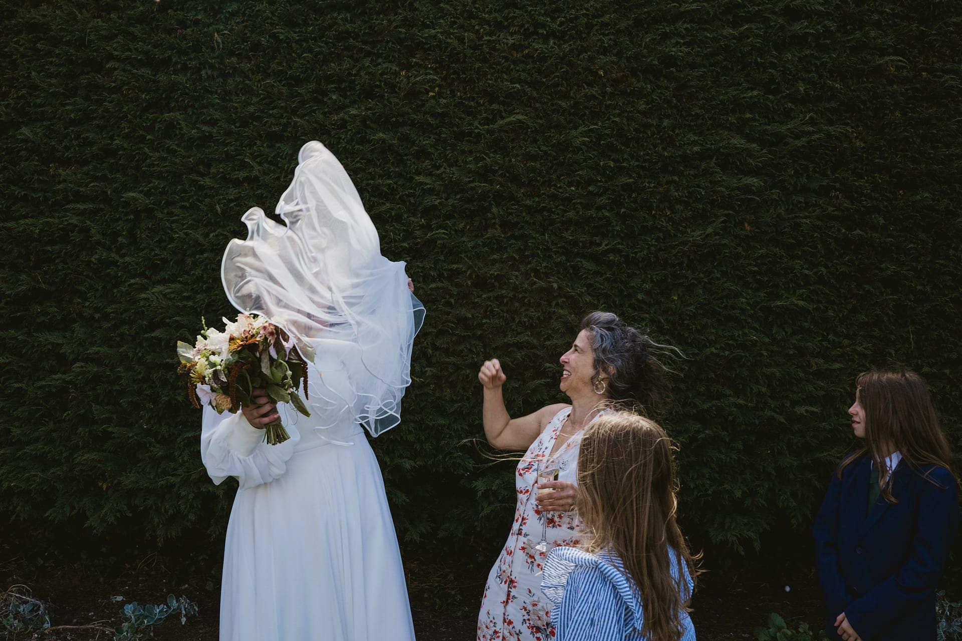 Bride's veil blowing in wind during outdoor celebration.
