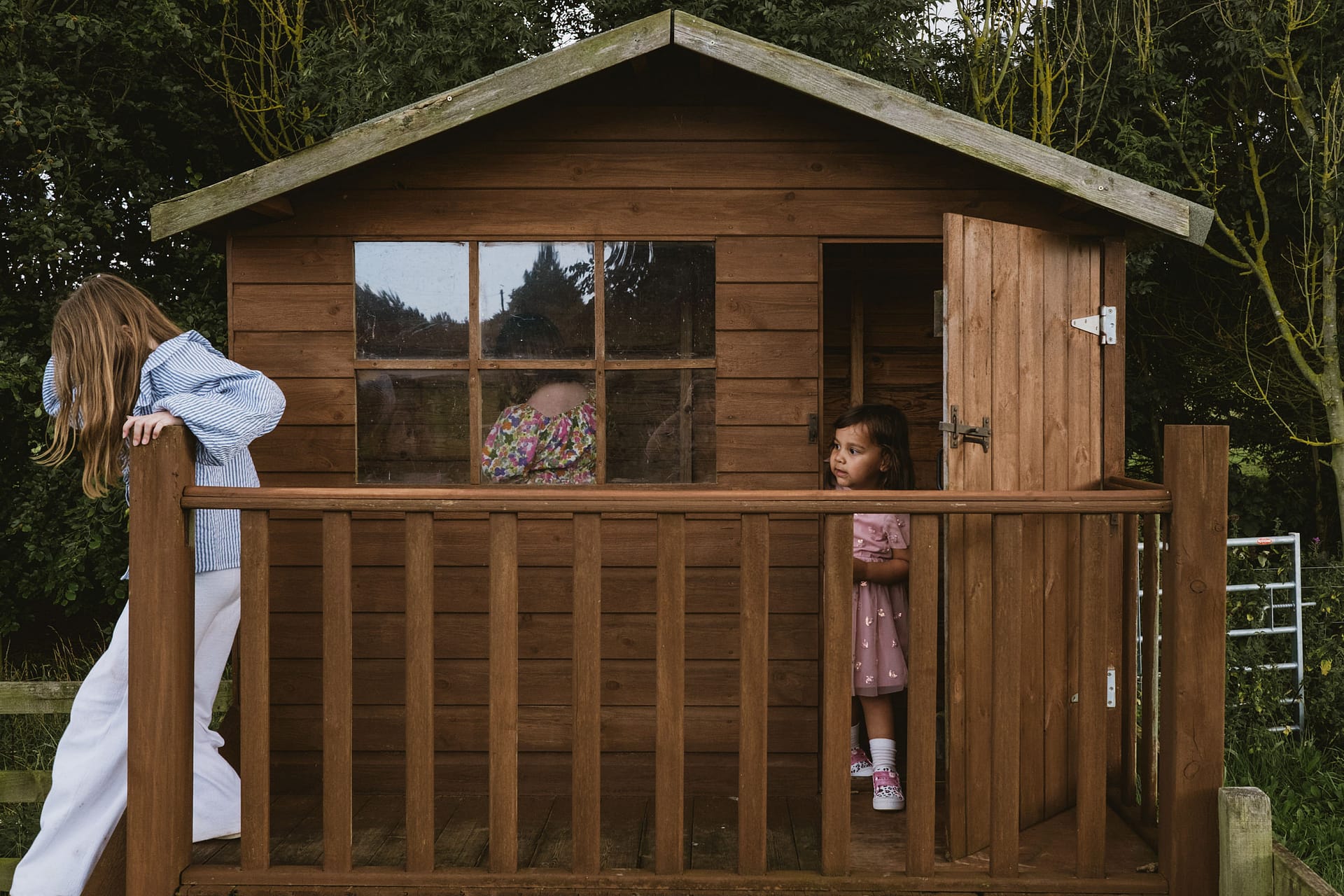 Children playing outside wooden playhouse in garden.