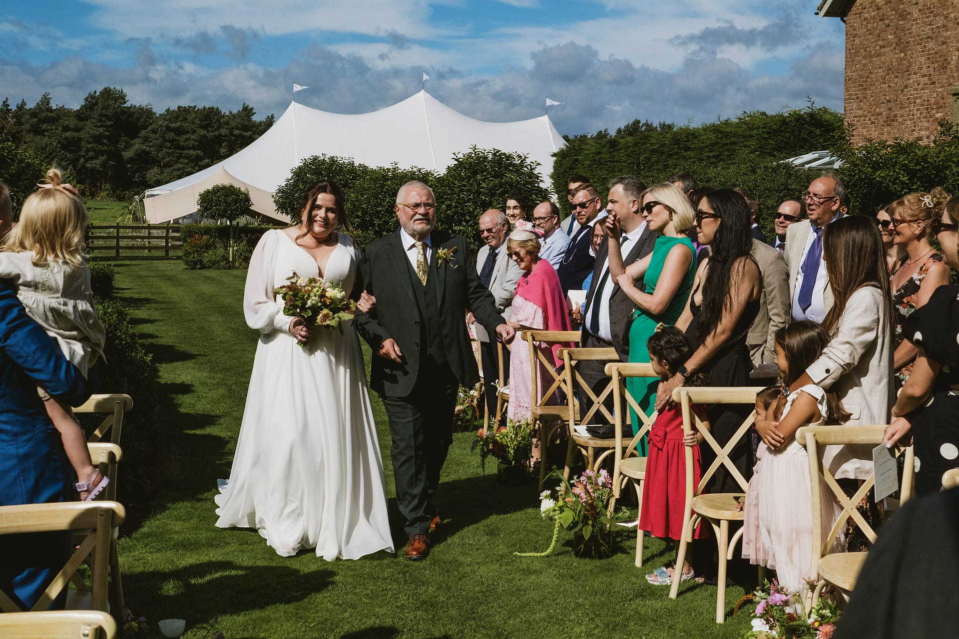 Bride walks down isle with father outdoors