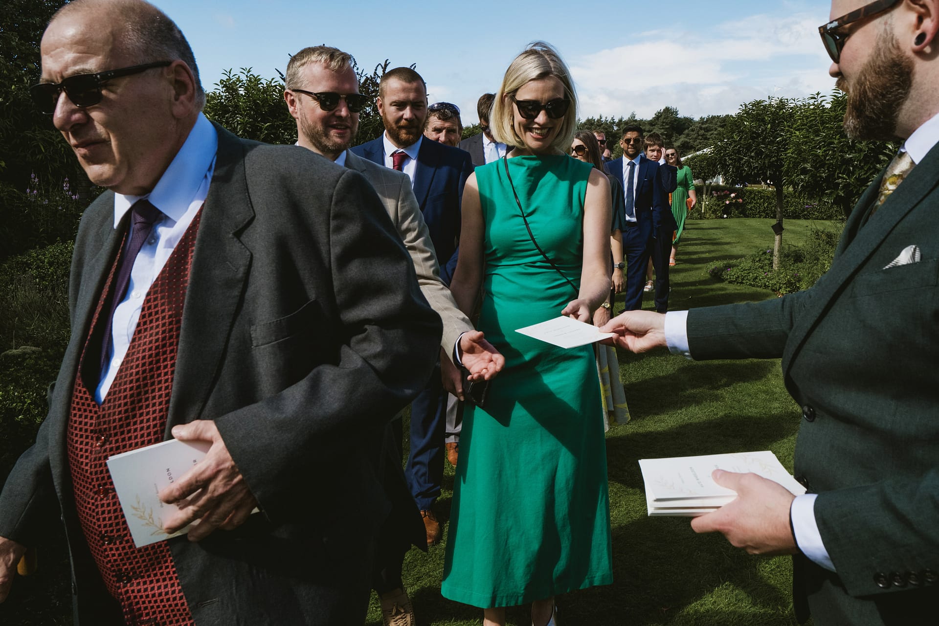 Guests receiving programmes at outdoor event.