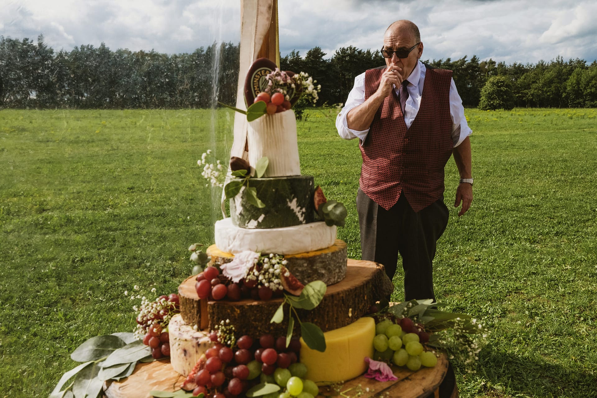 Man beside cheese wedding cake in outdoor setting