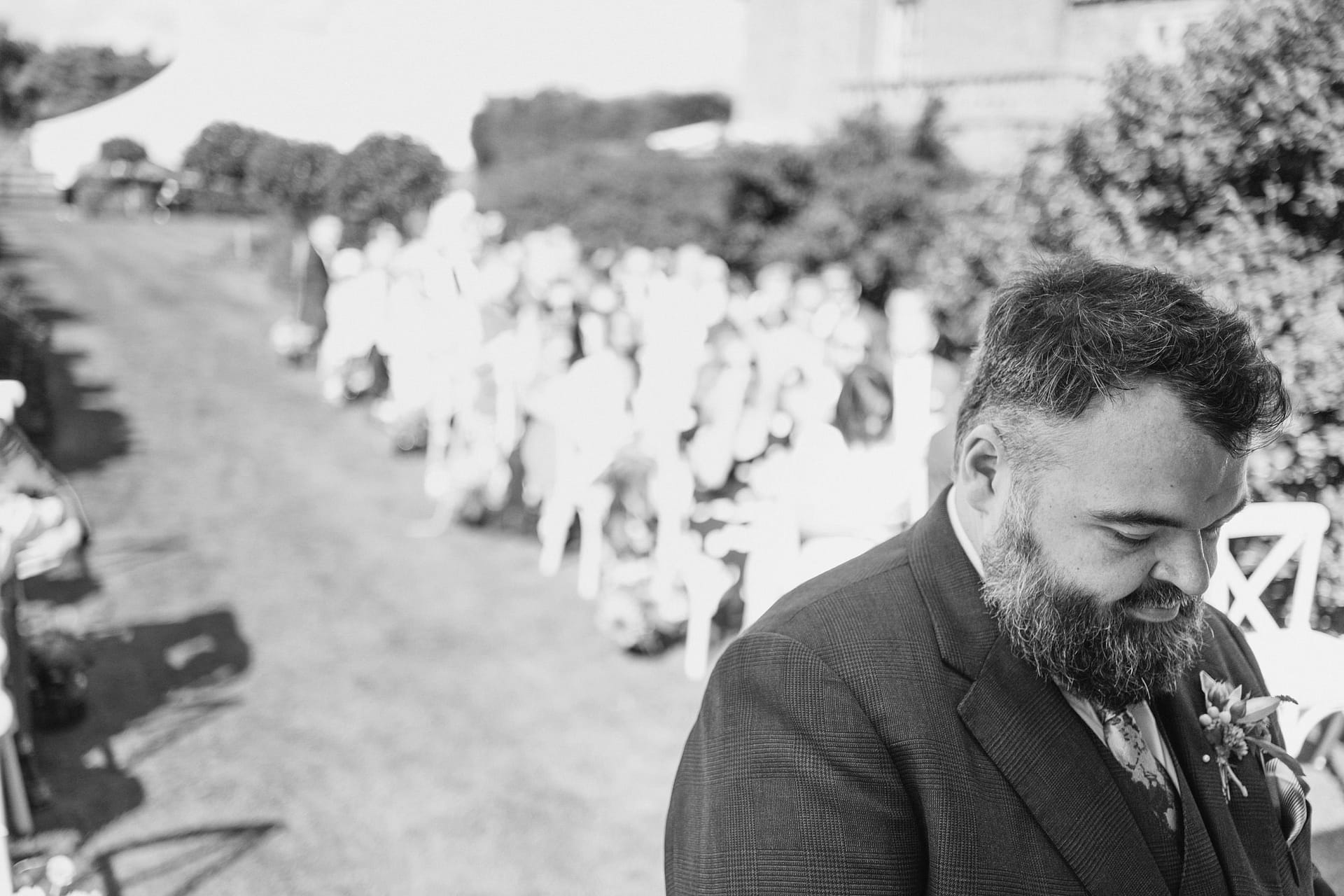 Man in suit at outdoor ceremony, crowd in background.