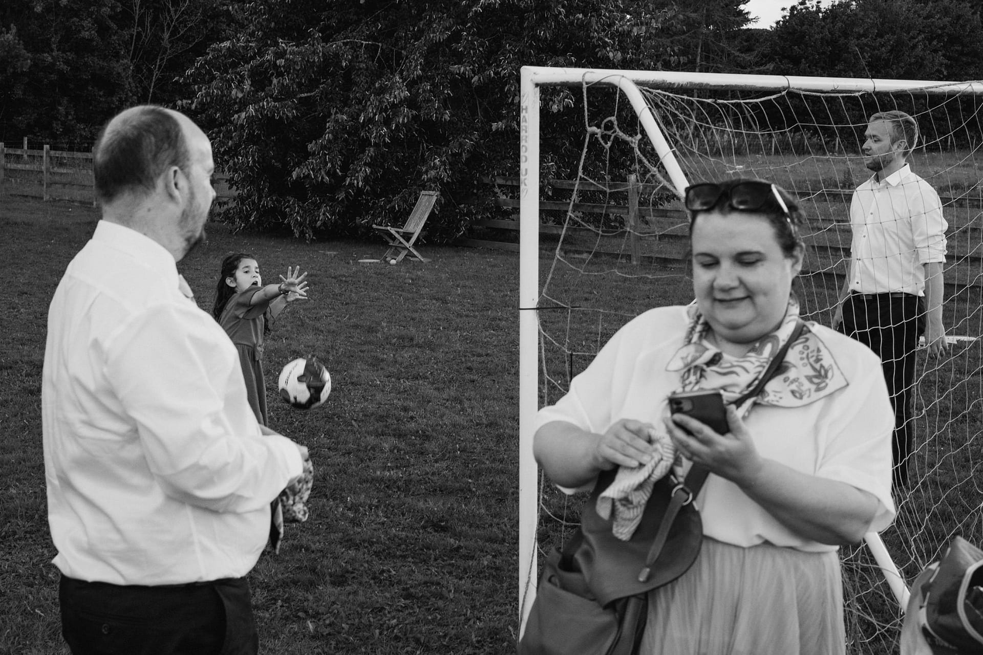 Group playing football in garden, one using phone.