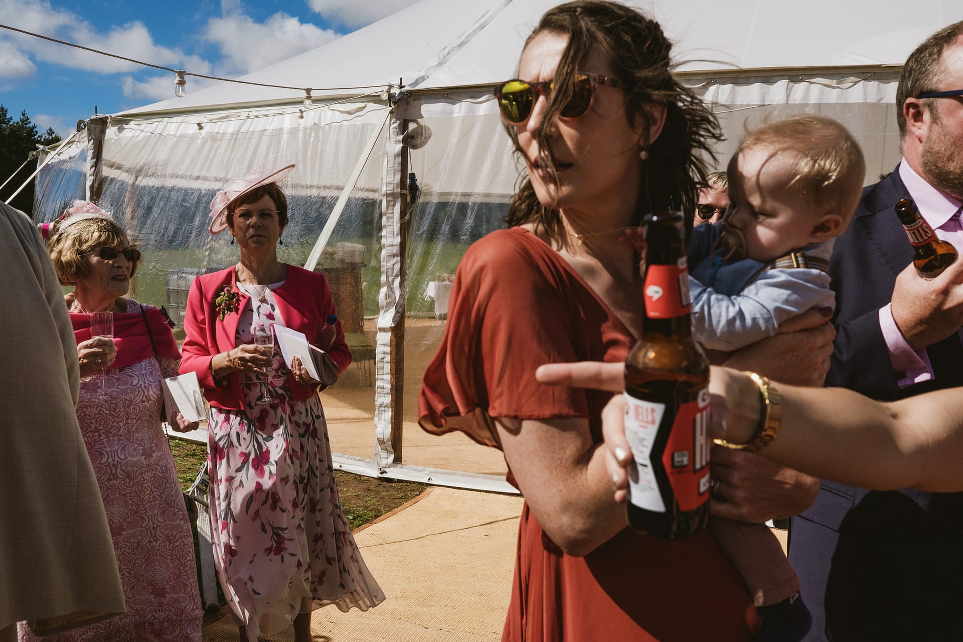 Outdoor wedding guests in formal attire, drinking beer