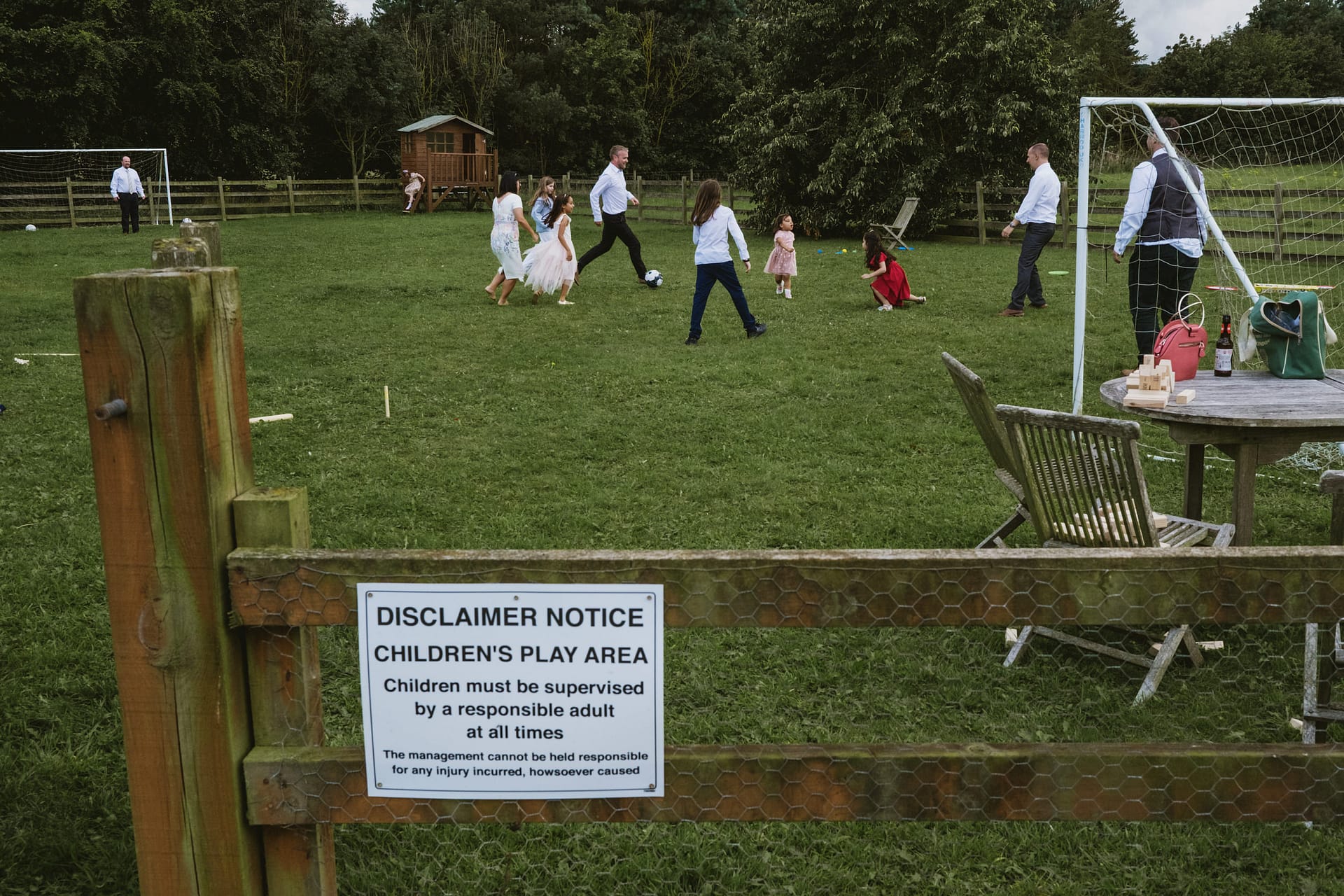 Children playing football in a park with adults.