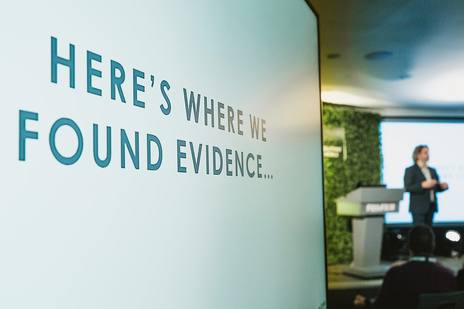 Corporate event photography & videography - speaker on stage is framed by the message on the screen during a conference