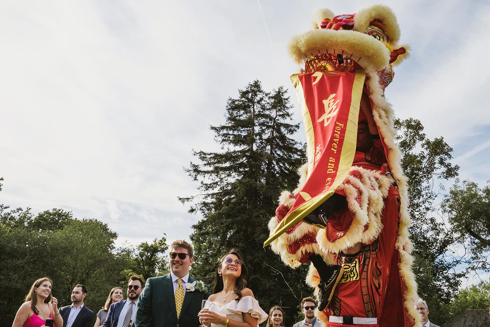 Bride, groom and guests stand beside a traditional Chinese lion at a wedding as a banner is unveiled