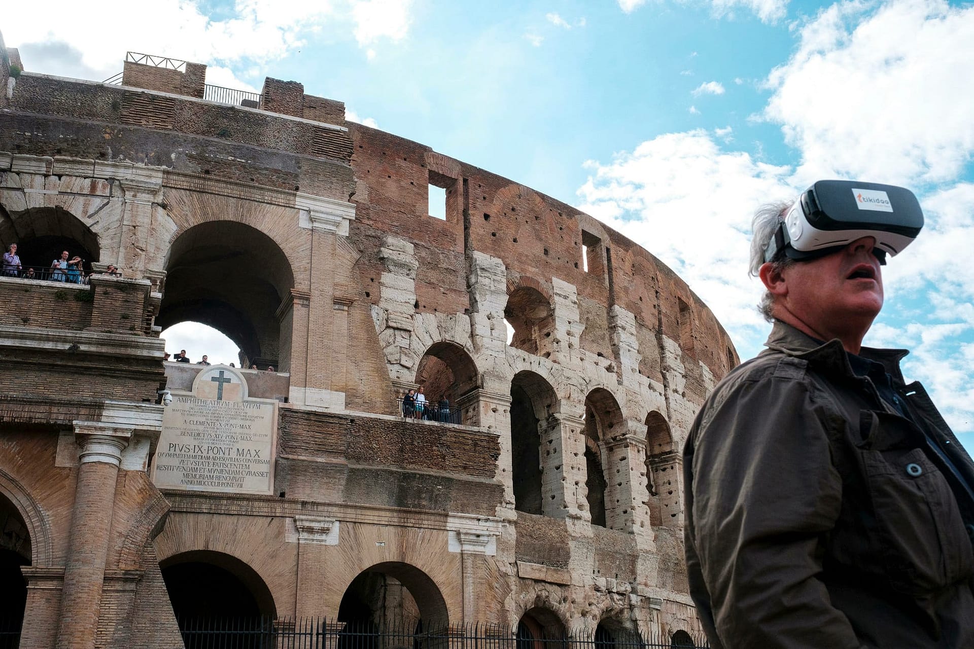 Street photograph captured in Rome, Italy. A man wearing a Virtual Reality headset is pictured looking in the opposite direction of Rome's famous Colosseum