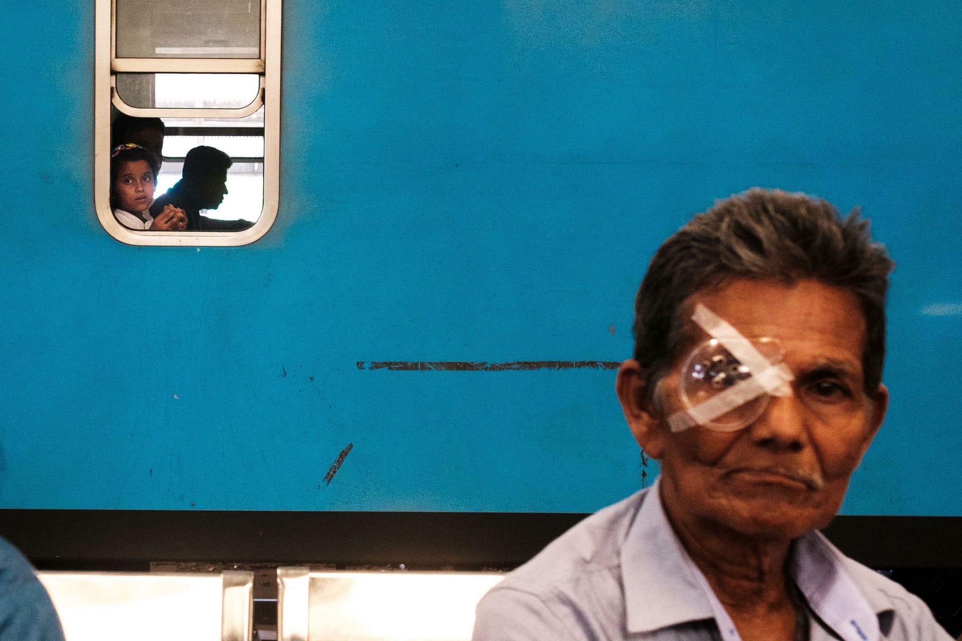 Street photograph captured in Columbo, Sri Lanka. A black line on a train links up with an "arrow" of tape, holding a form of monocle to the figure in the foreground's face