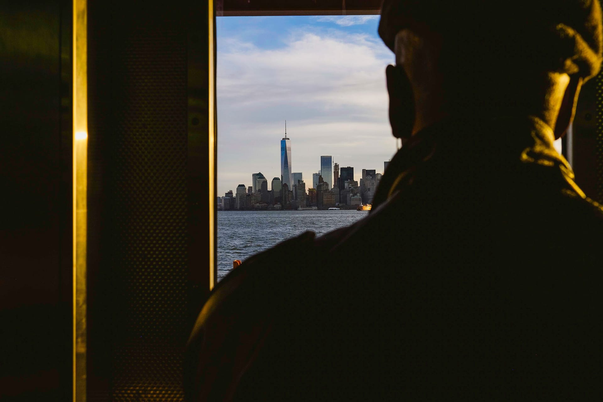 Street photograph captured in New York, USA. Man looks through the window of the Staten Island Ferry, looking on to the Manhatten skyline.