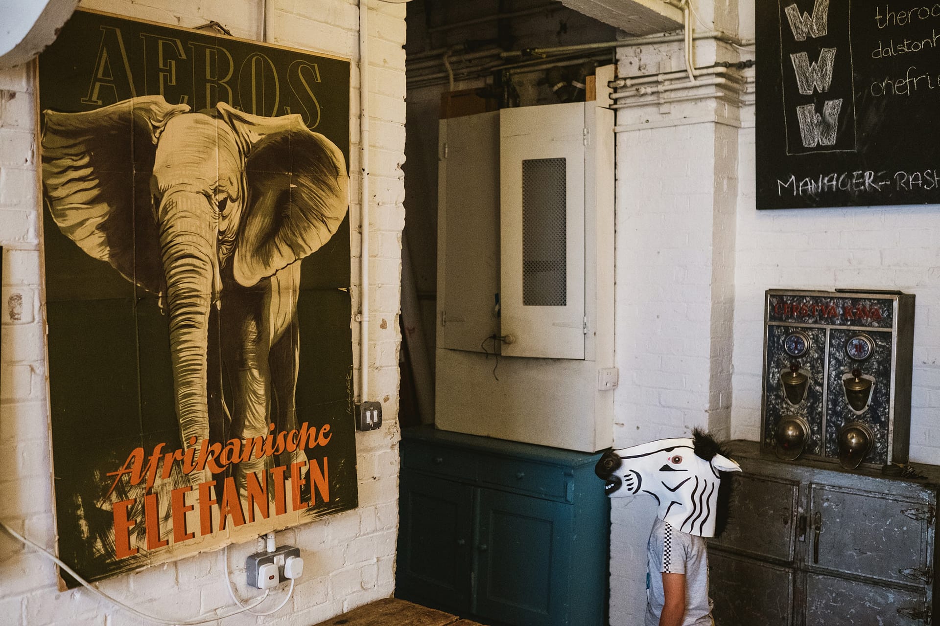 Comedic documentary style wedding photograph. A boy in a zebra mask stares at a painting of an elephant