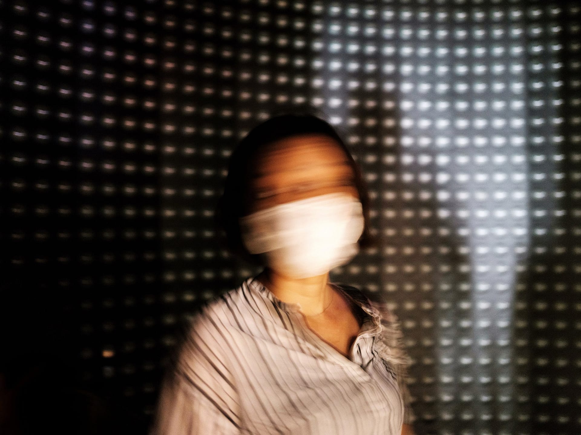 Street photograph captured in Tokyo, Japan. Woman in a medical face mask is photographed with motion blur as she moves her head side to side