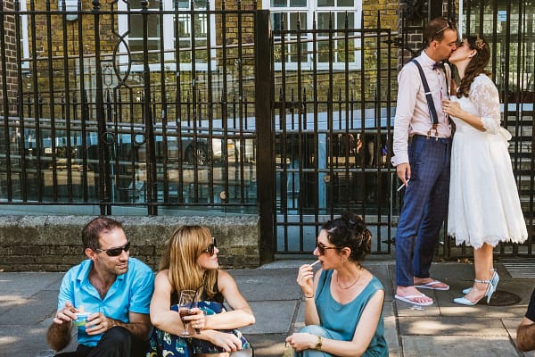 Wedding couple kissing, friends chatting outdoors.
