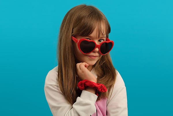 Studio portraiture by Kaleid from York Place Studios. Girl in bright pink sunglasses poses characterfully in front of a blue background