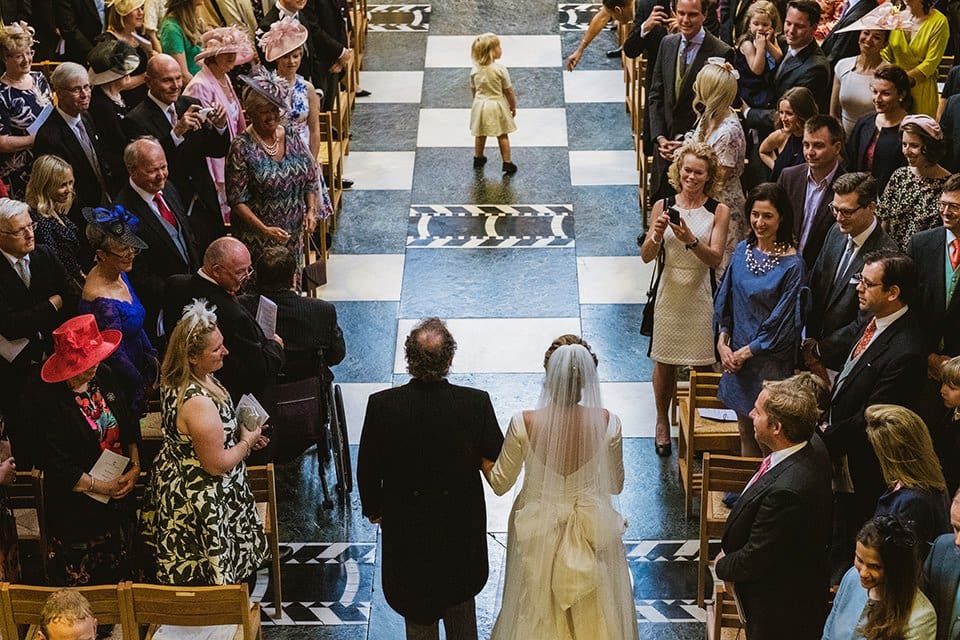 Bride and father walk down the aisle of Liverpool Cathedral, as young child runs into the aisle to join them. Wedding live streams from York Place