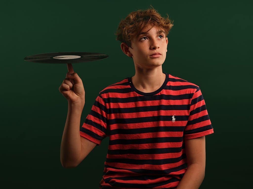 studio photography by kaleid.me teenager posing in front of a dark green background balancing a vinyl on his finger