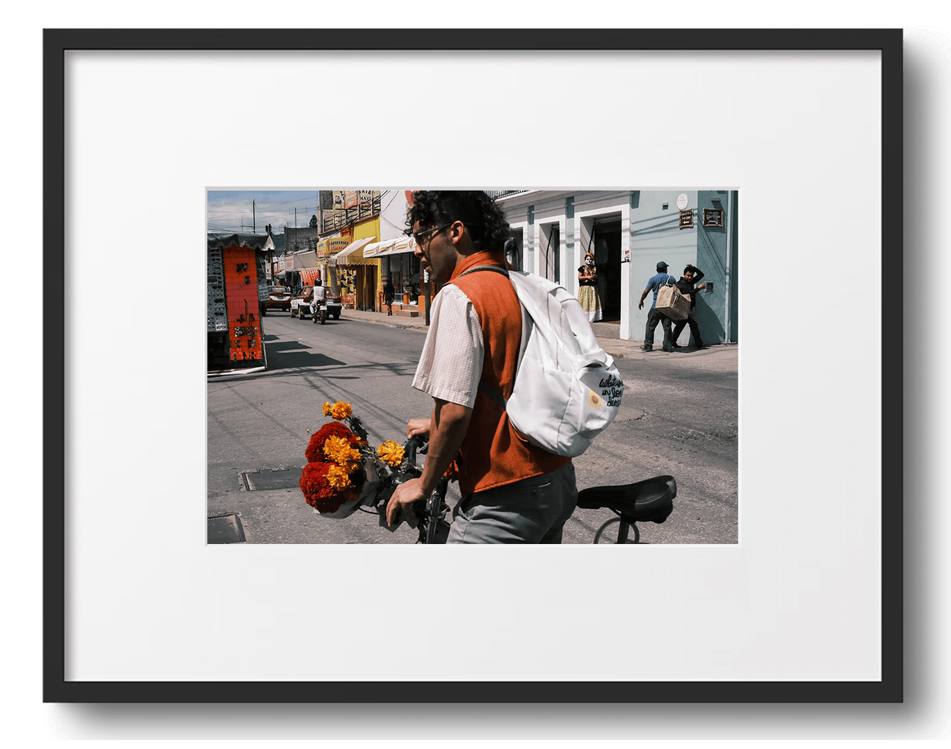 Cyclist with flowers on vibrant street scene in Oaxaca, Mexico. In the background two pedestrians collide, watched by a mysterious woman in skeletal makeup and flowers