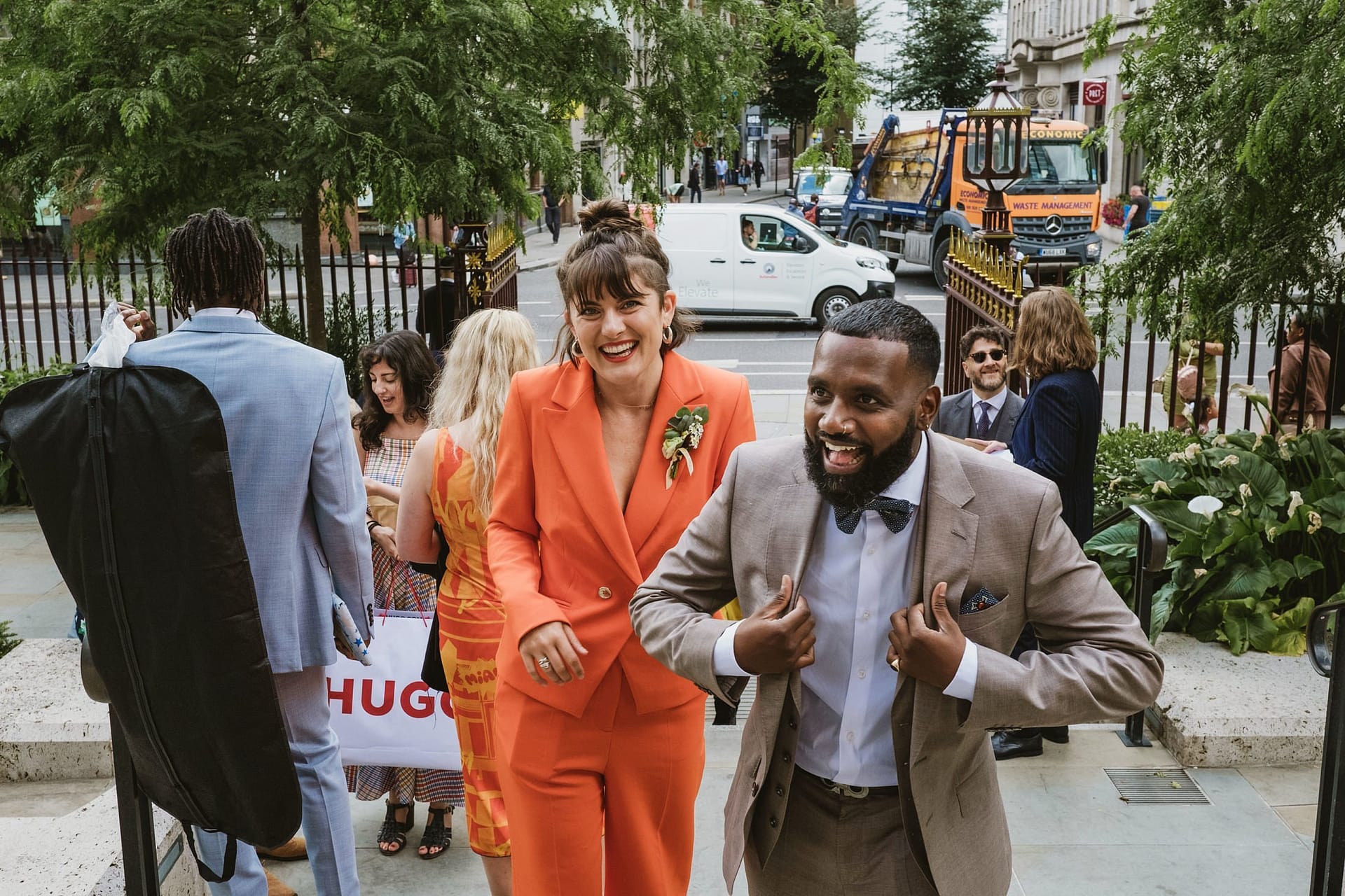 A man in an orange suit and a woman in a suit walking down the street in St Botolph without Aldgate.