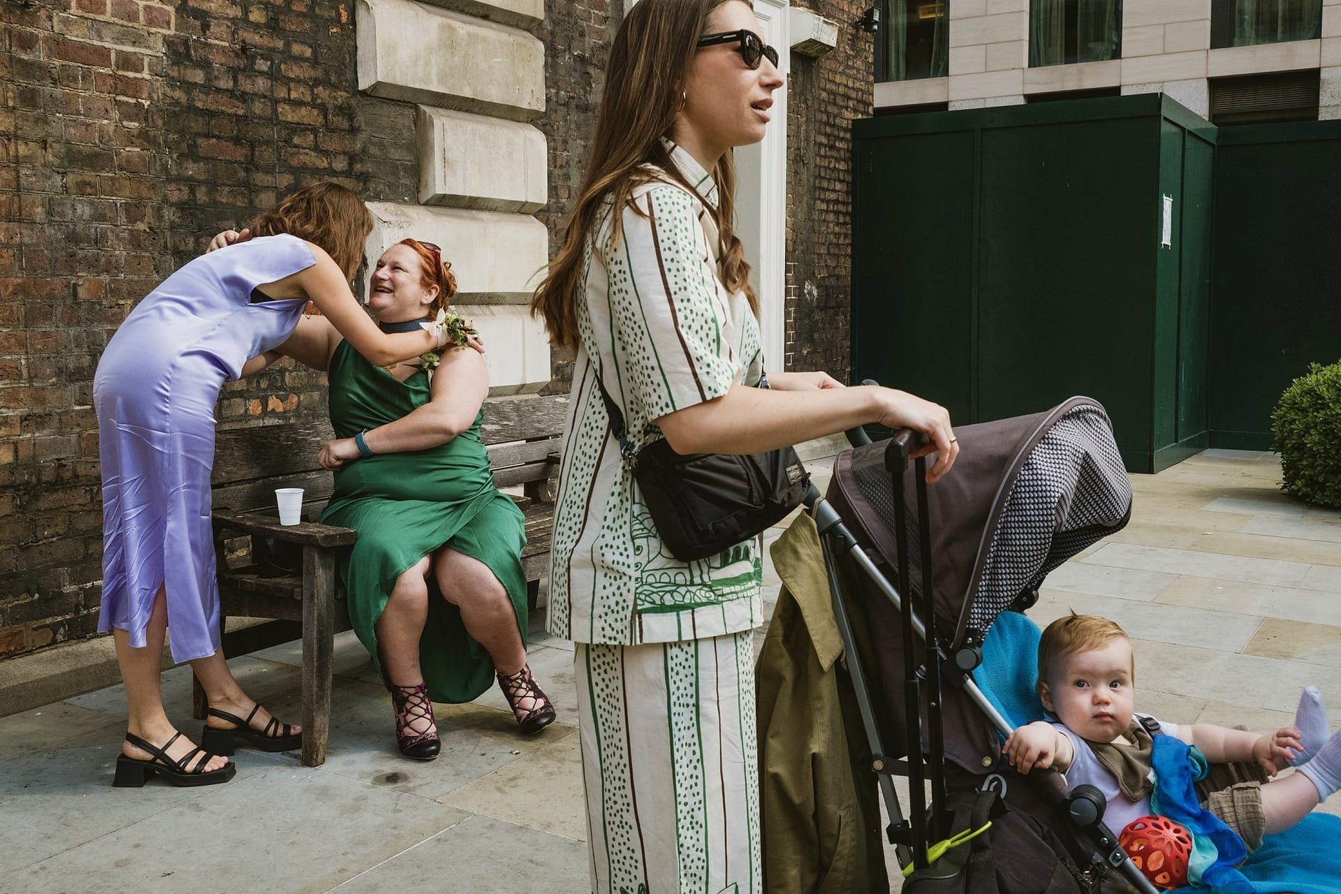 A woman in a green dress pushing a stroller with a baby through the streets of St Botolph without Aldgate.