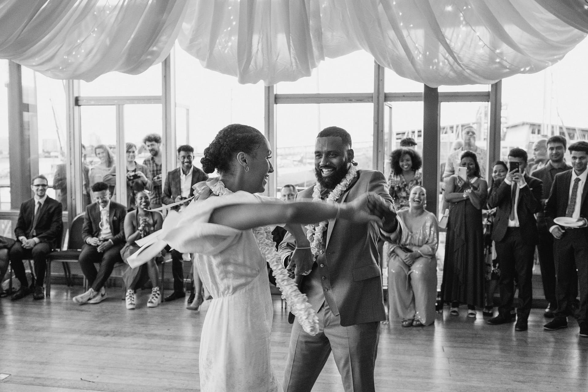 Greenwich Yacht Club Wedding Photography captures a couple gracefully dancing in a room, while surrounded by an audience of fascinated onlookers.