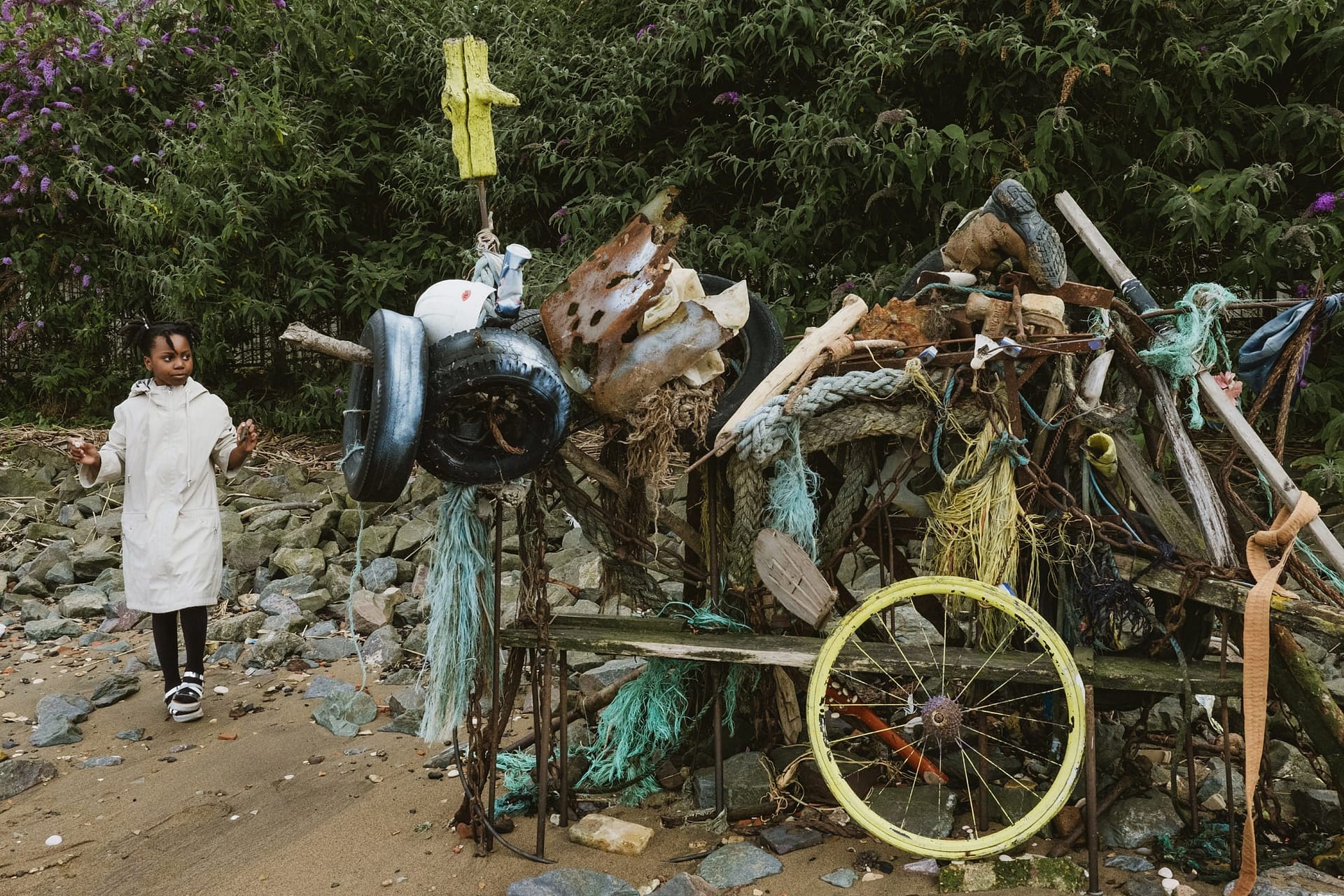 A little girl standing next to a pile of old things on the beach during Greenwich Yacht Club Wedding Photography.