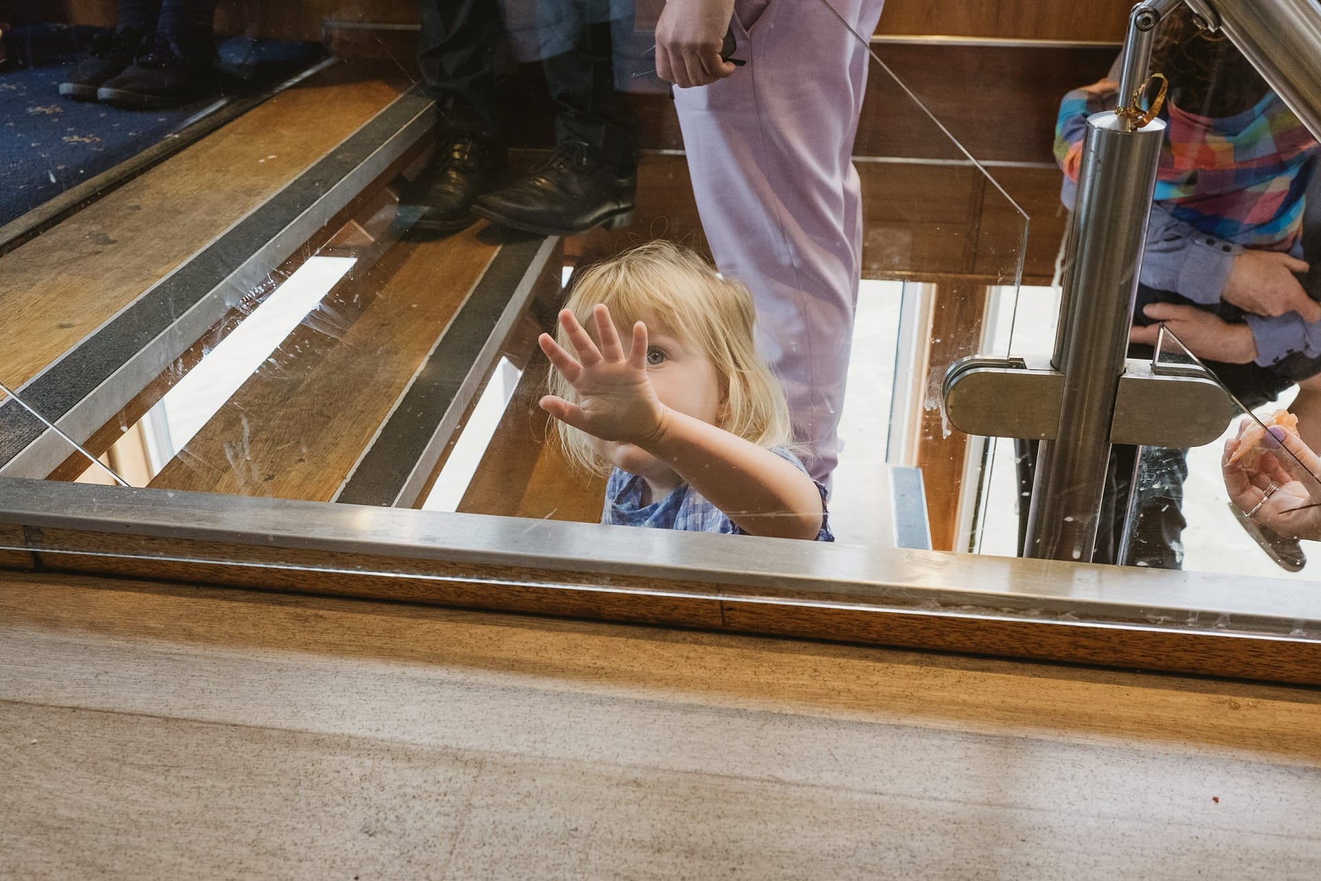 A child reaching out to the side of a glass door at Greenwich Yacht Club Wedding Photography event.