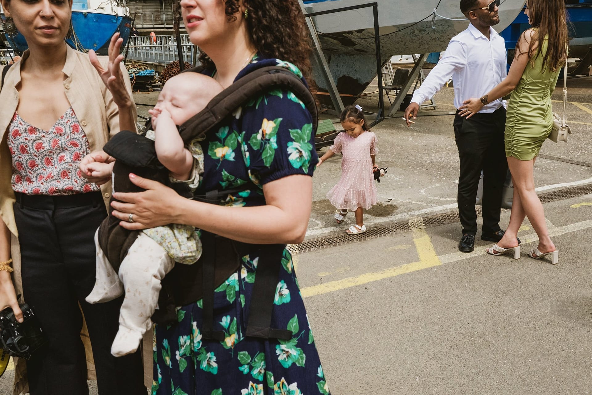 A group of people, including a baby in a carrier, standing near a boat at Greenwich Yacht Club.