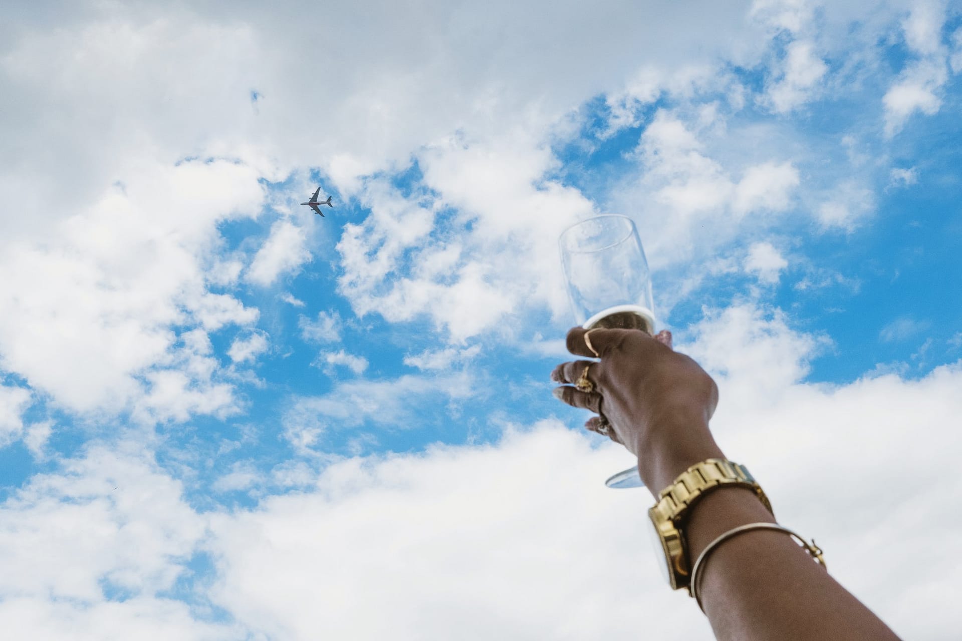 At the Greenwich Yacht Club, a woman elegantly holds a glass of champagne, creating a timeless moment against the backdrop of the beautiful blue sky and a plane.