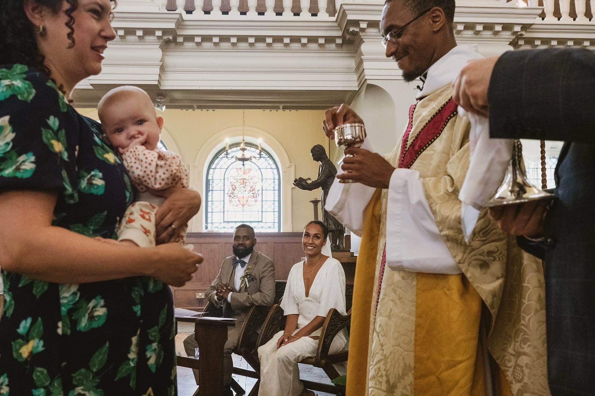 A Greenwich Yacht Club Wedding Photography priest is holding a baby in a church.