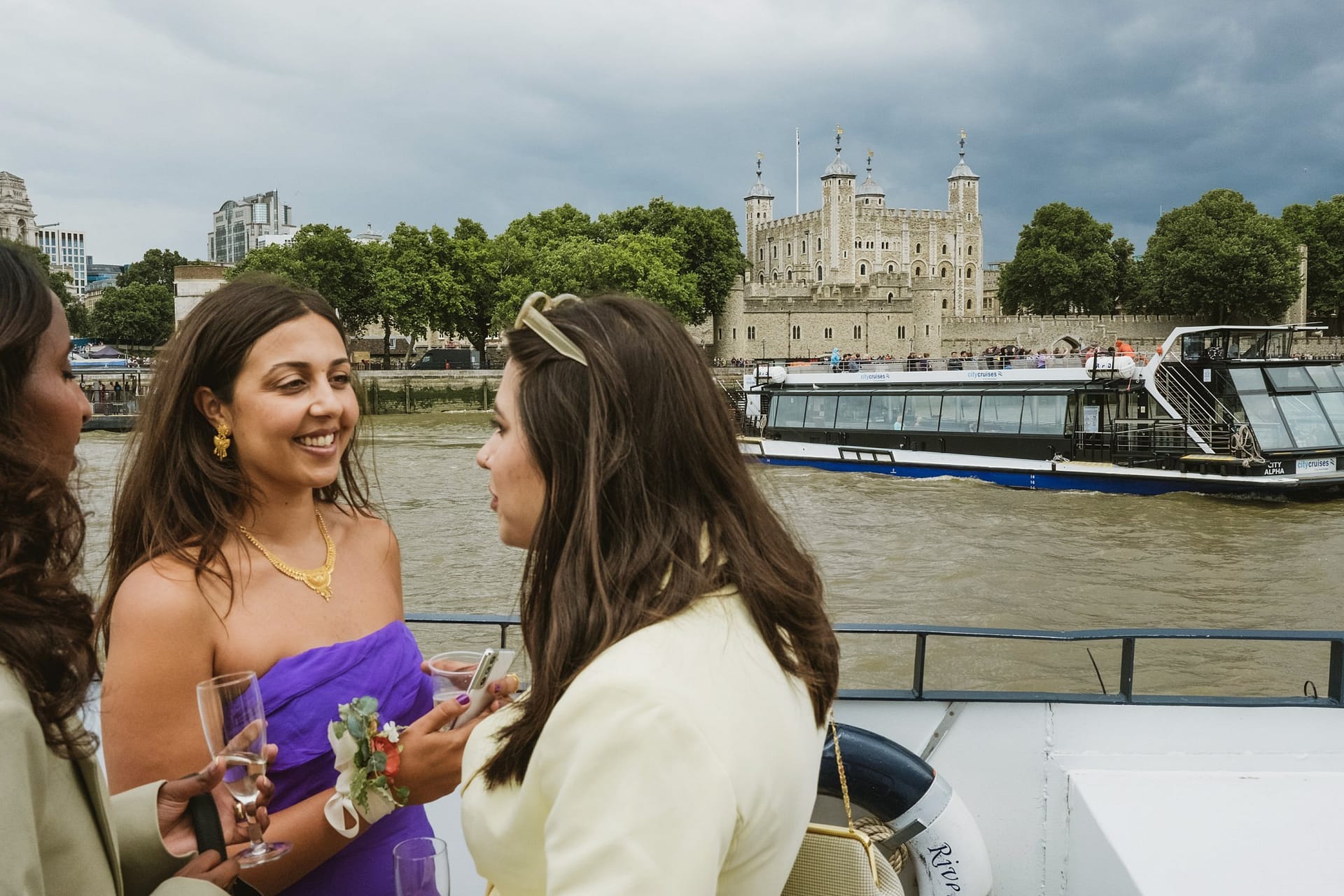 Three women discussing a Greenwich Yacht Club wedding on a boat with the Tower of London in the background.