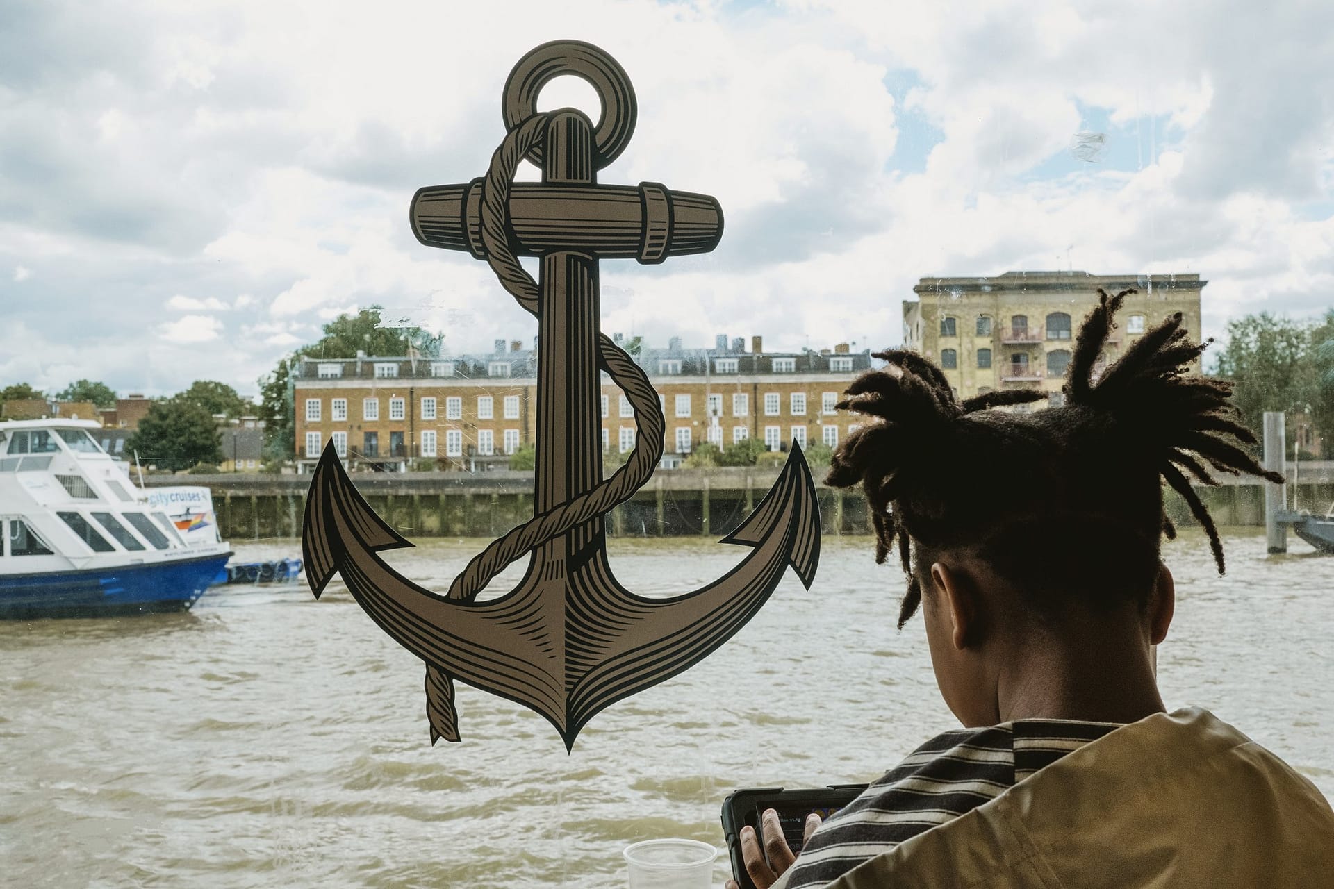 A girl with dreadlocks looking out over the water at Greenwich Yacht Club in London.