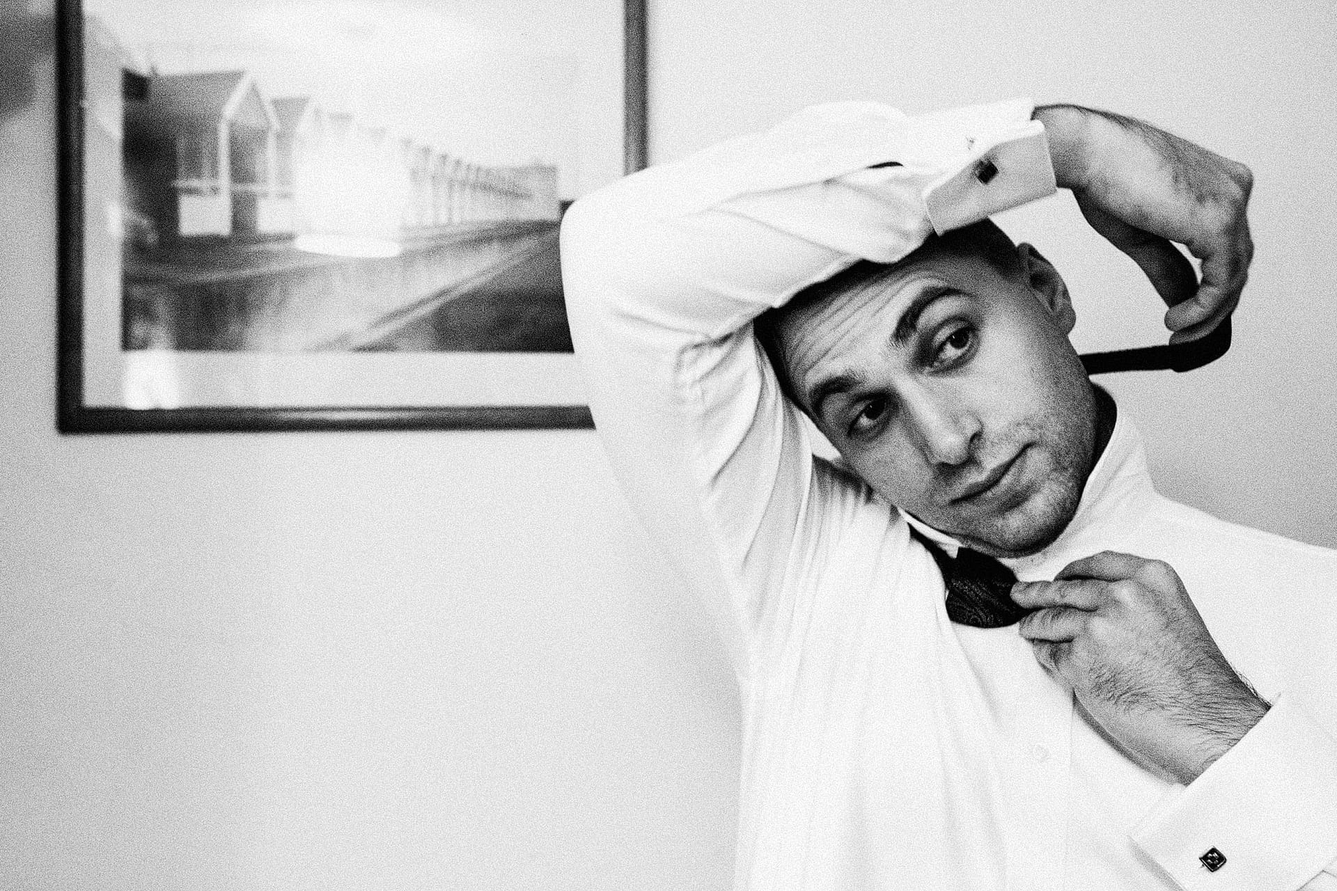 low-light wedding photography - groom ties his bow tie in preparation for his wedding. (Monochrome Image)