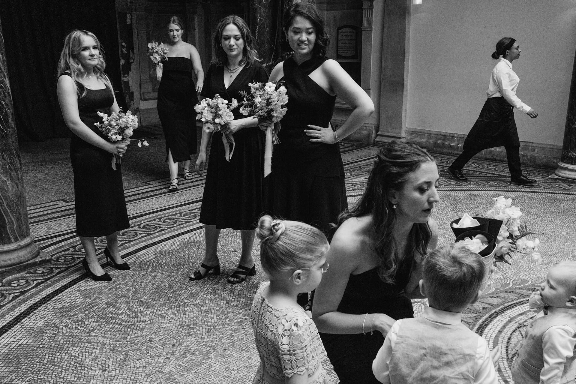 Bridesmaids with bouquets, children gathered, formal setting.