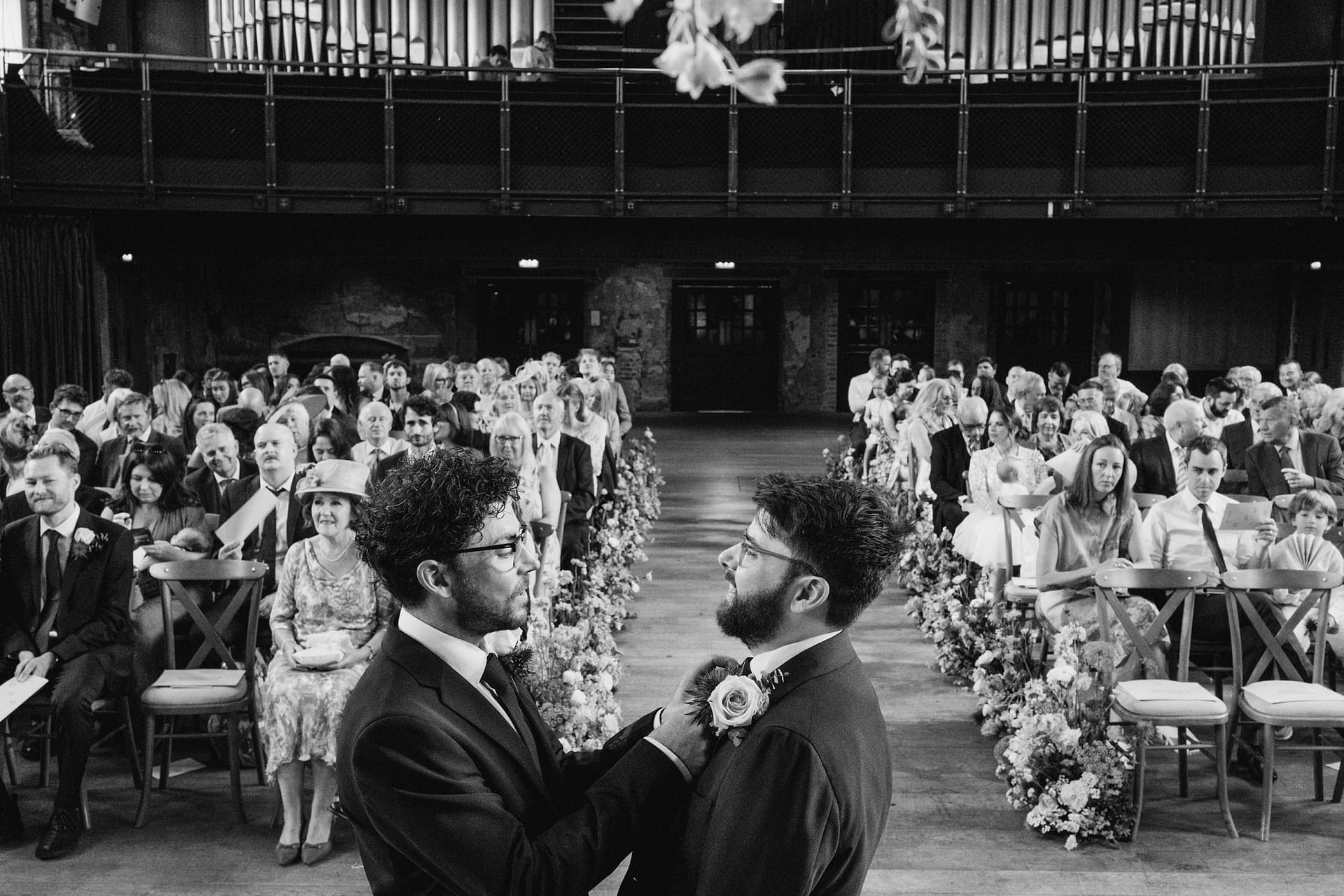 Groom adjusts partner's boutonniere at wedding ceremony.