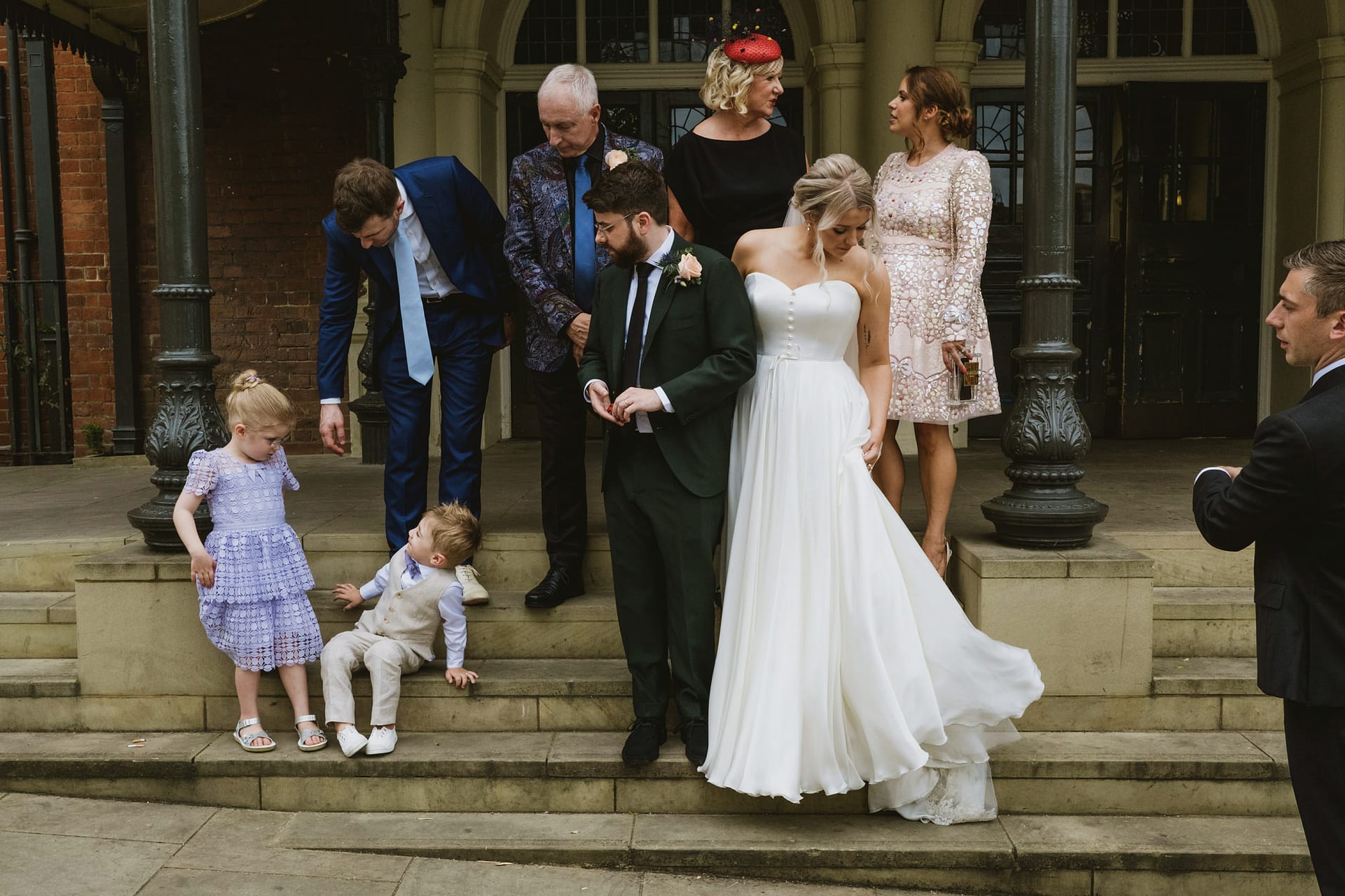 Wedding group photo on steps, bride in white dress.