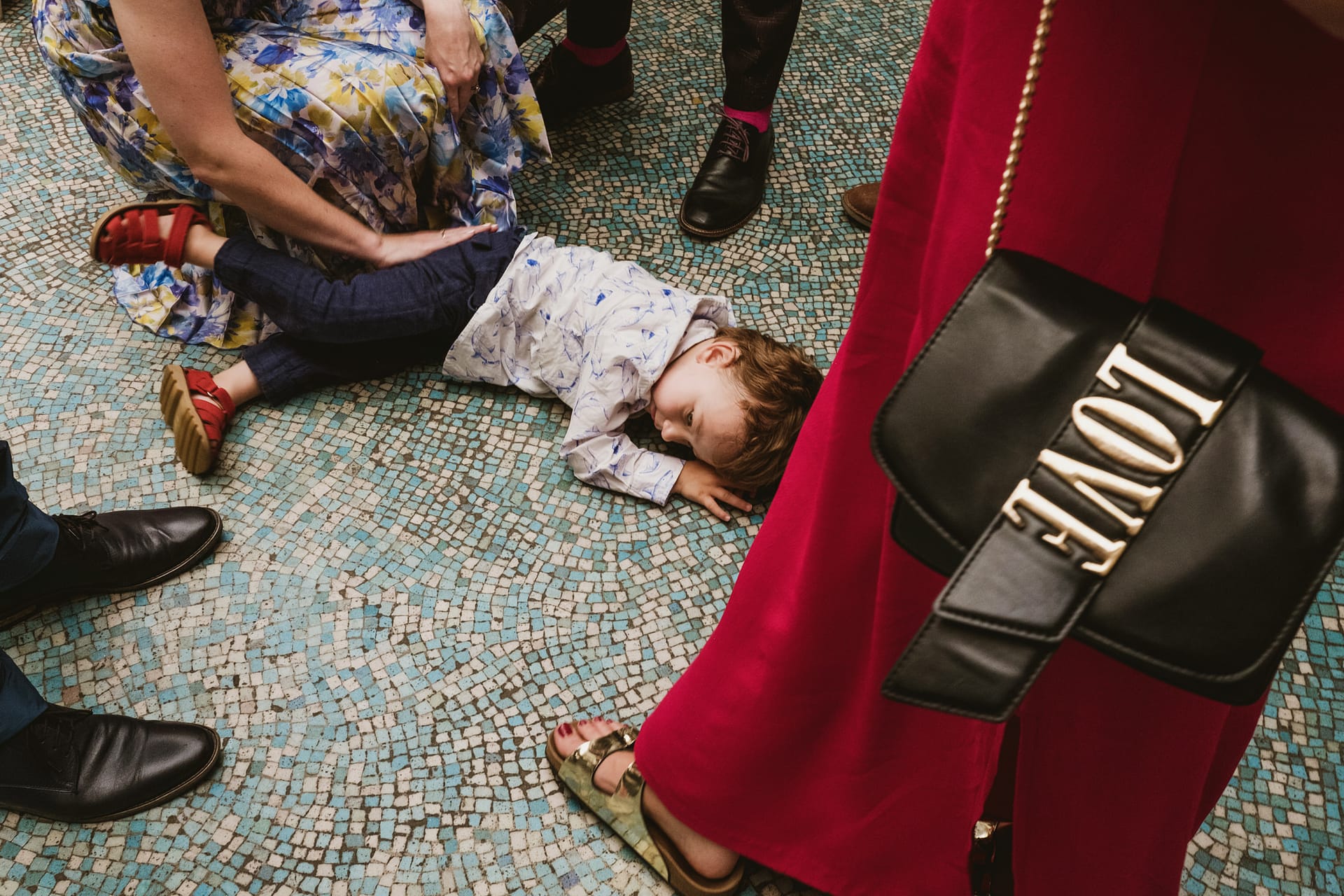 Child lying on mosaic floor at formal event.