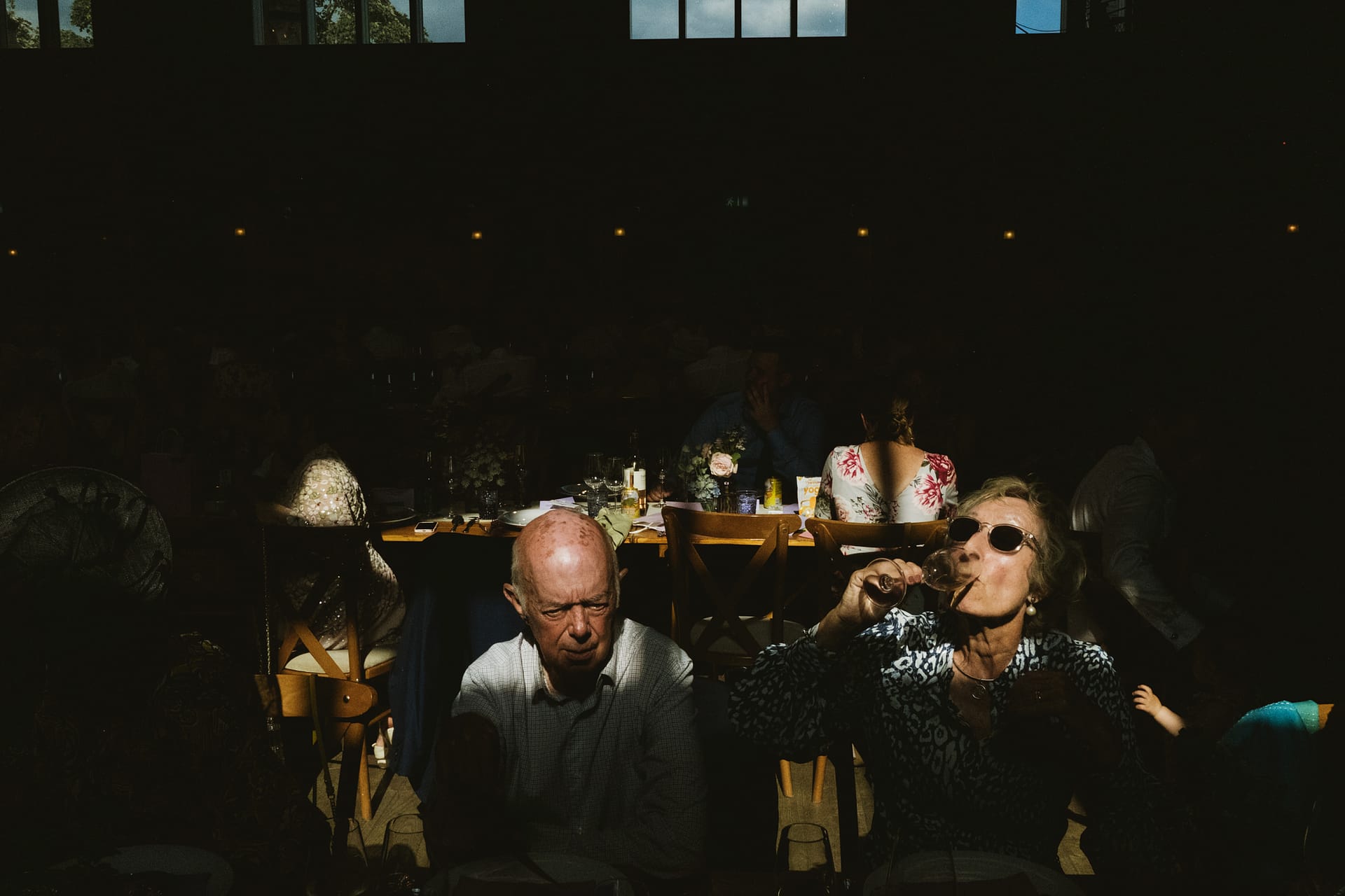 People at dimly lit indoor event, woman sipping wine.