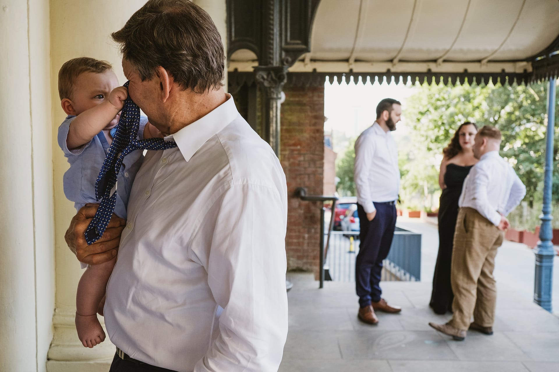 Man holding baby with group talking in background.