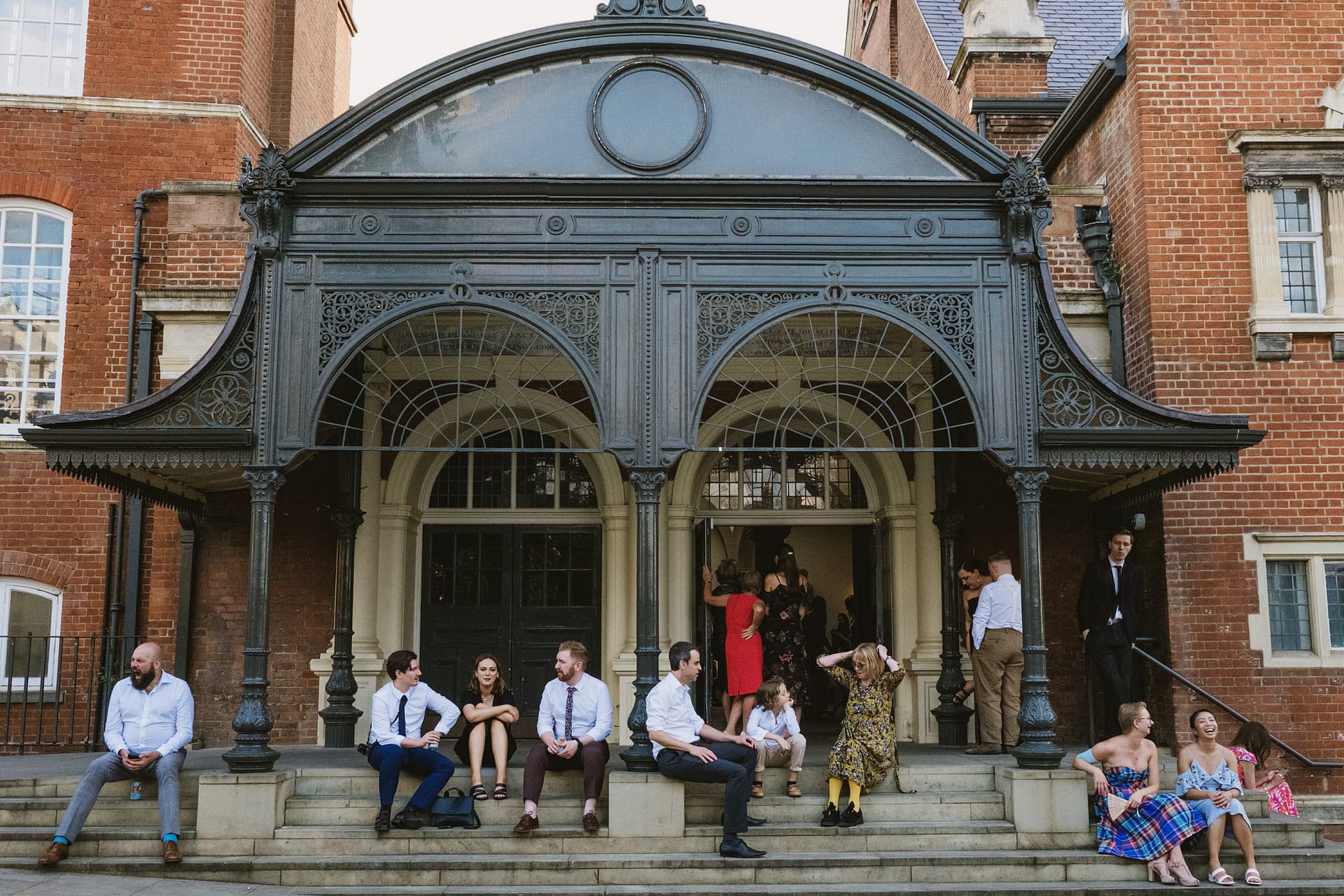 People sitting on steps outside historic brick building.