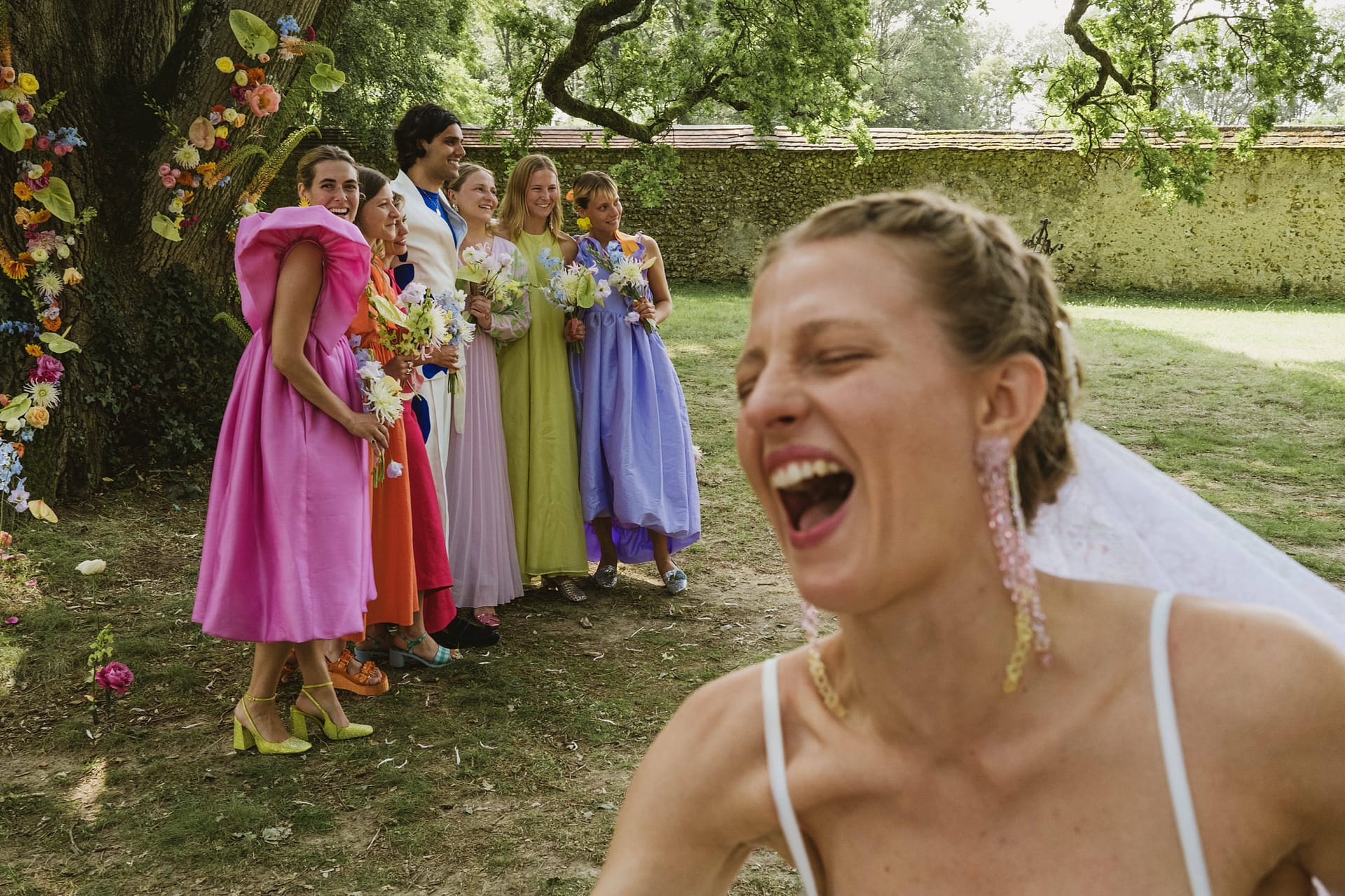 bride laughing hard whilst the groom and the bridesmaids have their group photo taken at Chateau du Fey in France