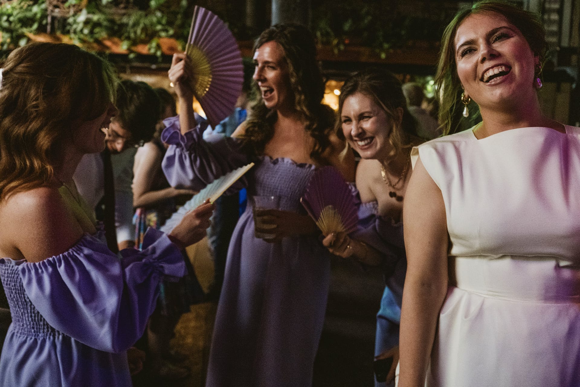 Women laughing and using hand fans at event.