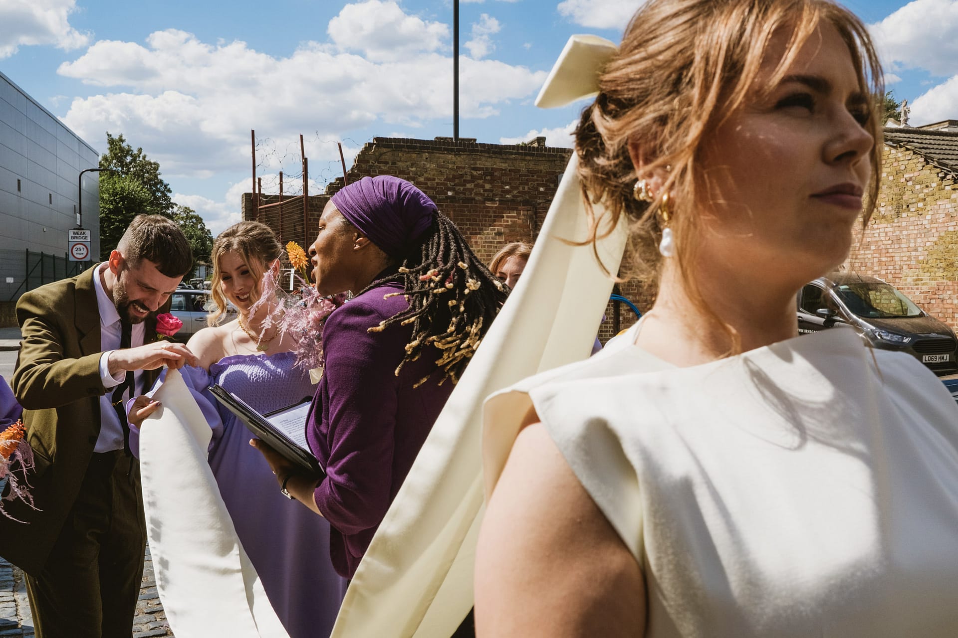 Wedding party interacts outdoors in colourful attire.
