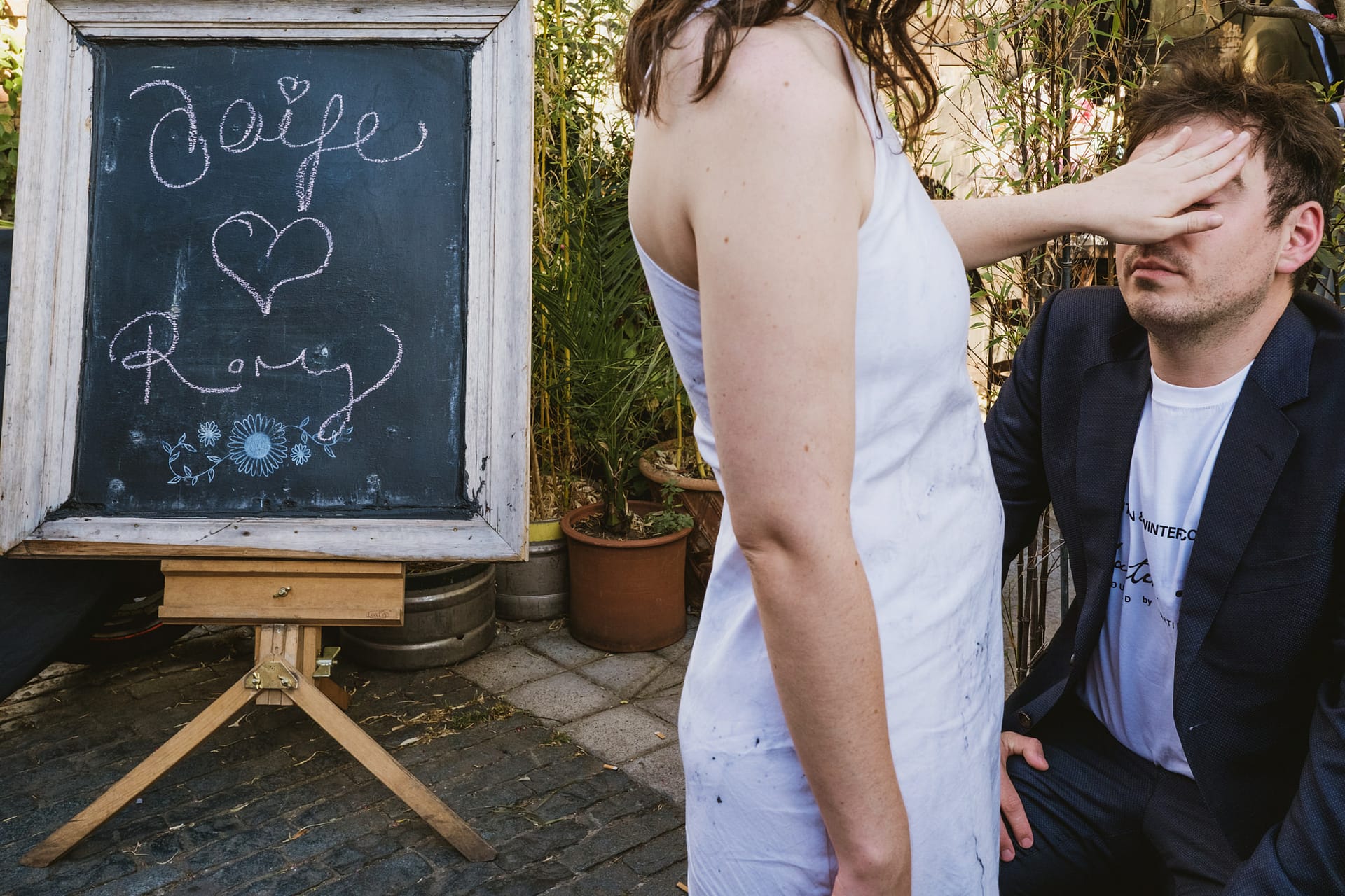 Man kneeled, woman covering his eyes, chalkboard message