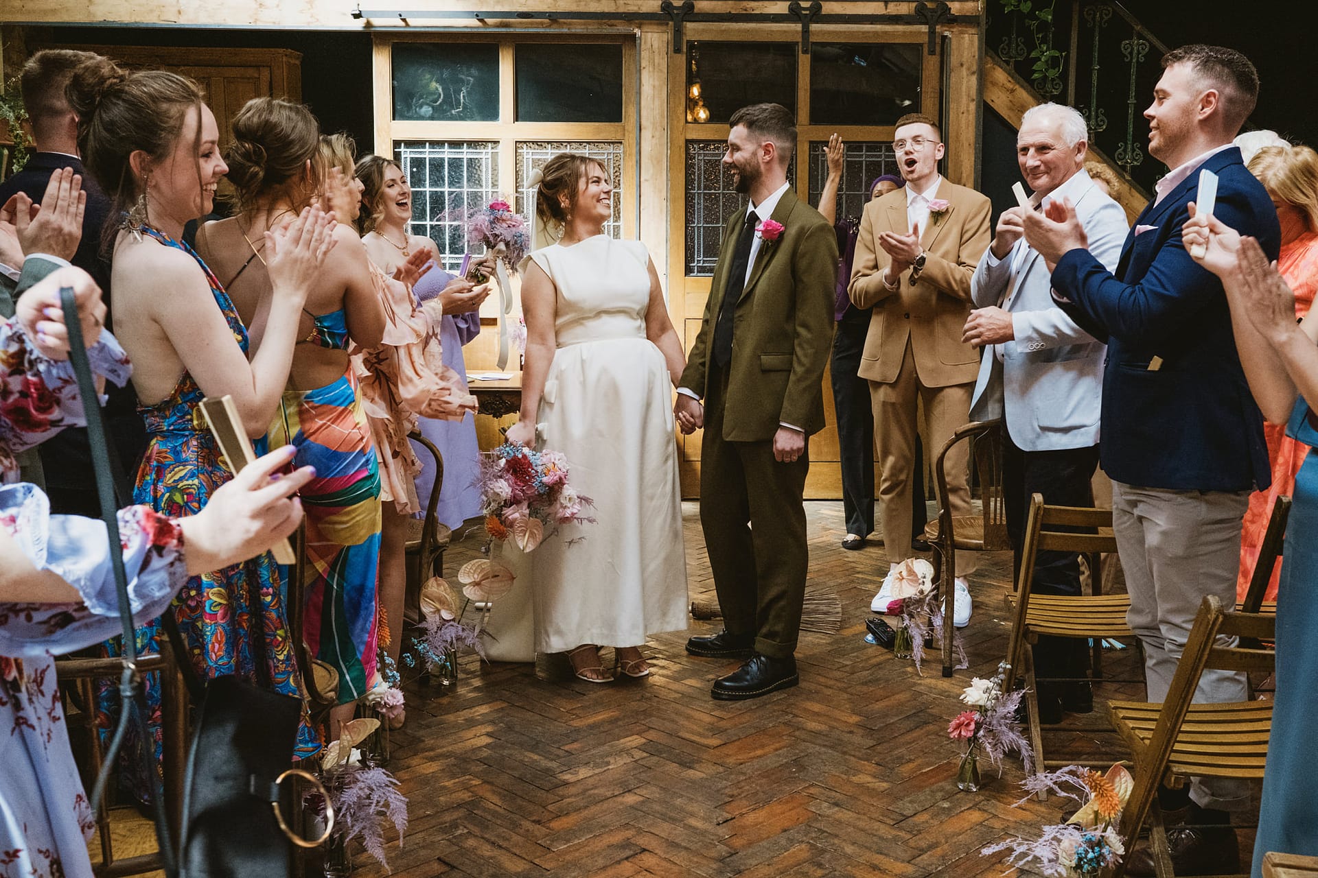 Bride and groom exit amid applause at rustic wedding.