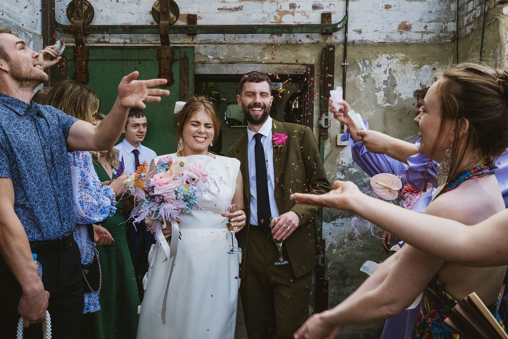 Wedding couple smiling with confetti and friends around